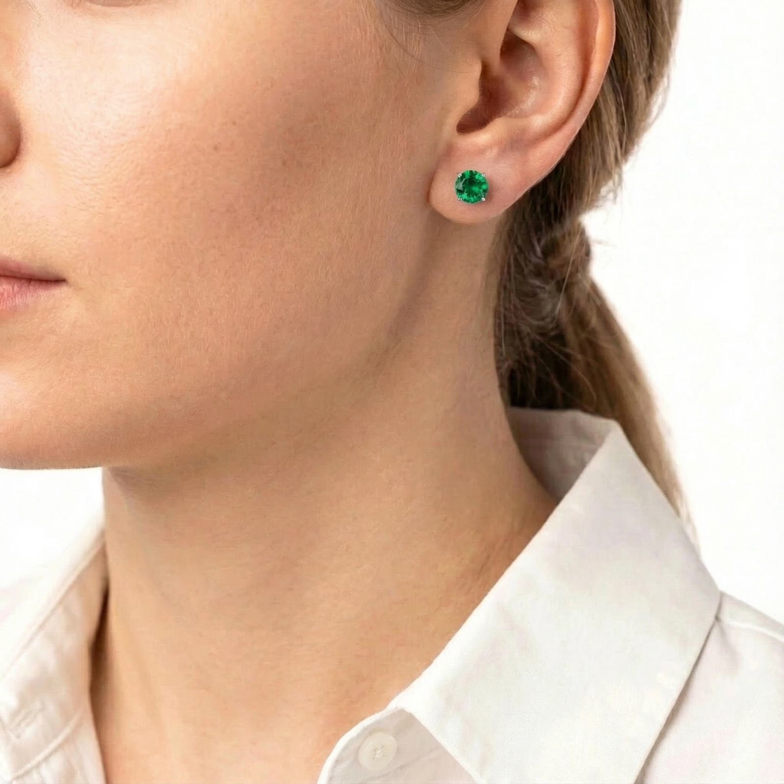 Side profile of a woman wearing a round-cut simulated emerald stud earring in sterling silver.