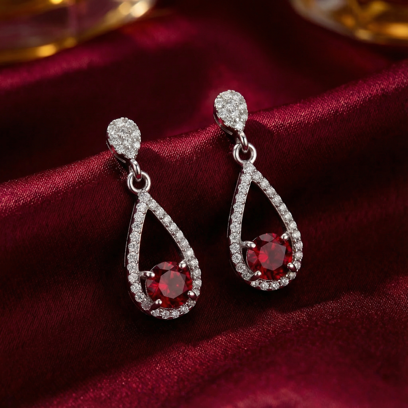 Teardrop S925 sterling silver drop earrings with round simulated rubies on red silk fabric.