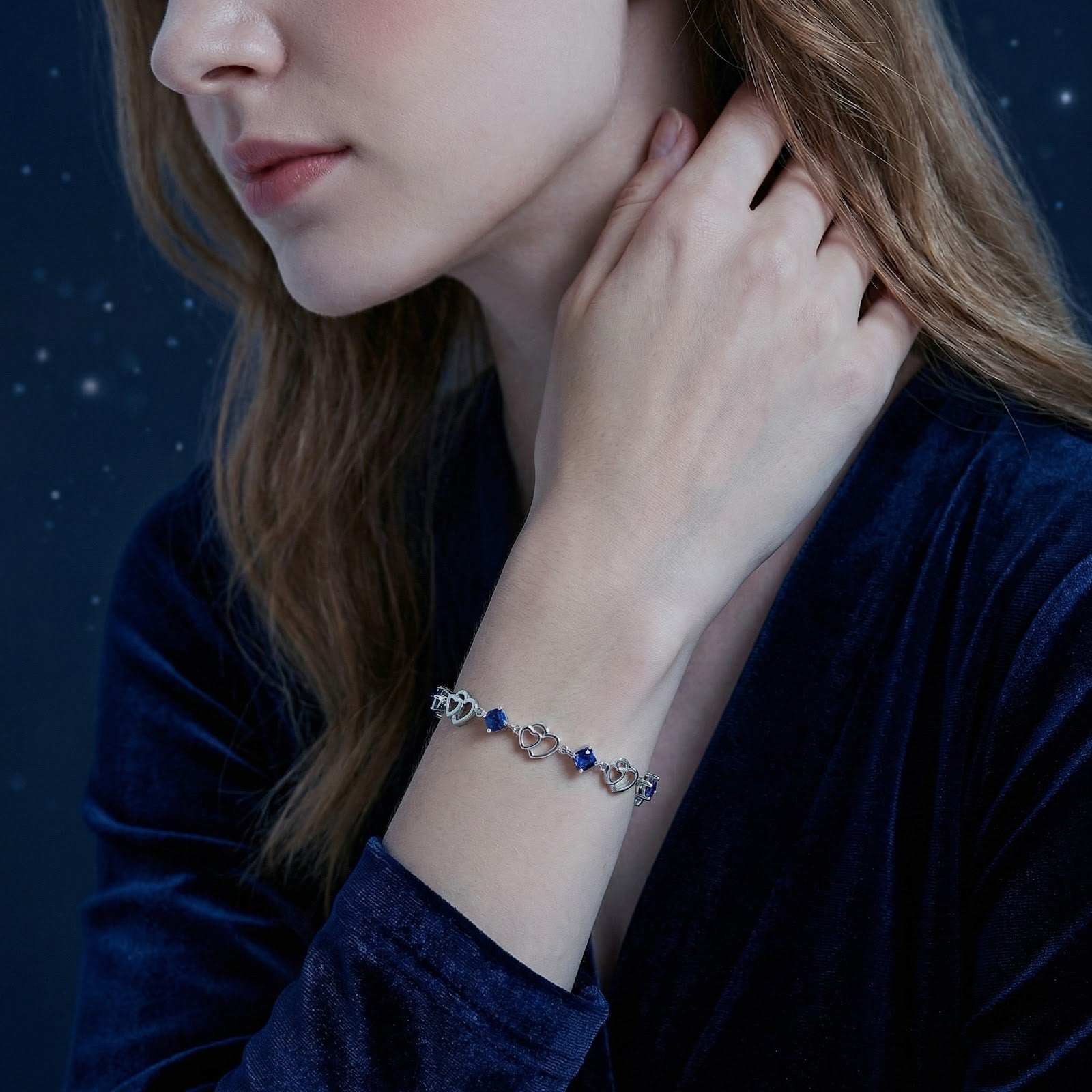 Woman in a blue velvet dress wearing the S925 sterling silver Celestelle heart bracelet with blue simulated sapphires.