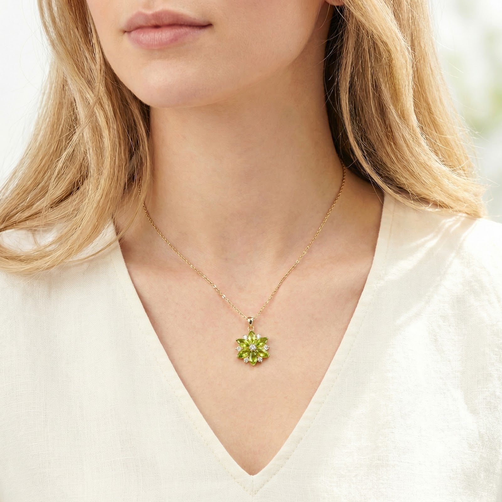 Gold stainless steel floral necklace with green simulated peridot stones worn by a model in a white linen top.