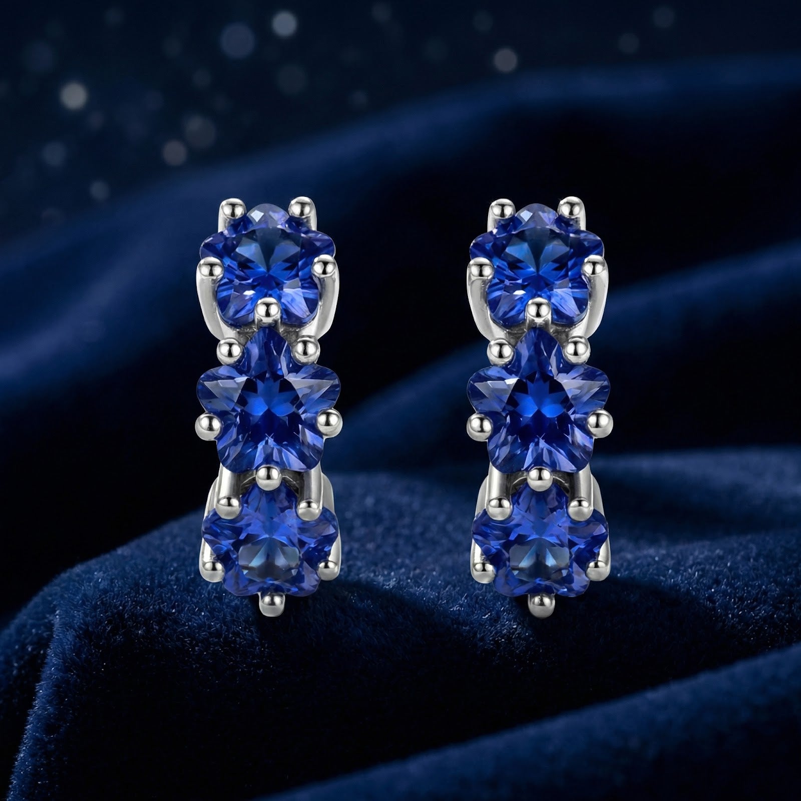 Front view of sterling silver star huggie earrings featuring three star-cut royal blue simulated sapphires.