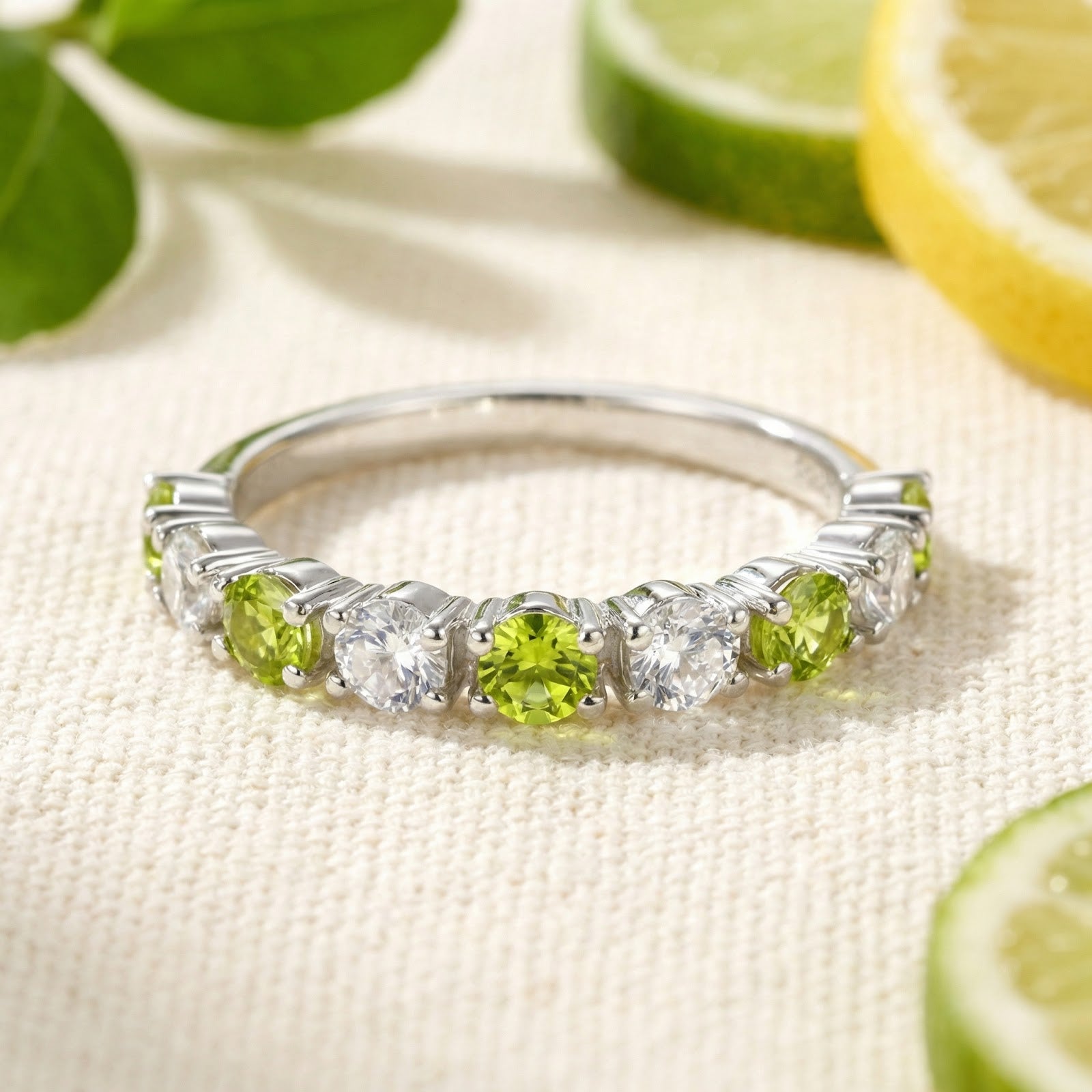 Sterling silver ring with round-cut simulated peridot and clear stones on a textured surface with citrus fruit.