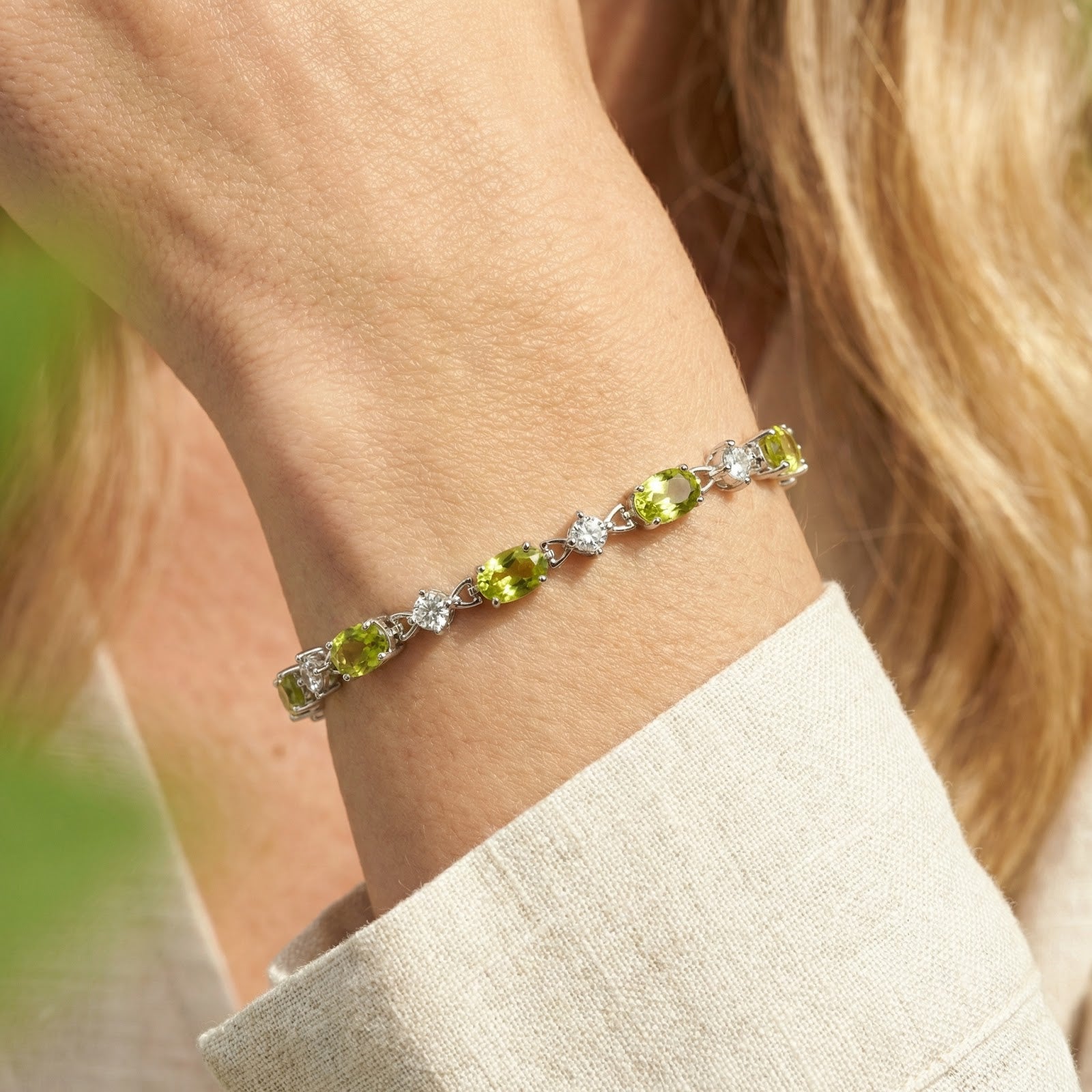 Close-up of oval-cut simulated peridot and round clear stones on a sterling silver station bracelet.