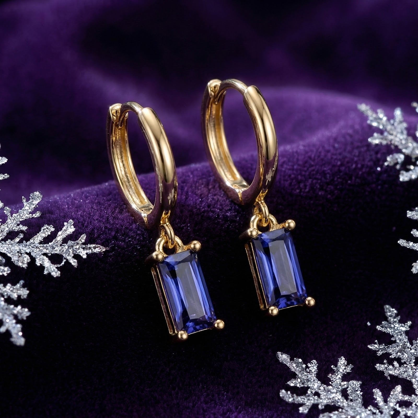 Macro view of emerald-cut simulated tanzanite drop earrings in 18K gold vermeil on a purple velvet surface.