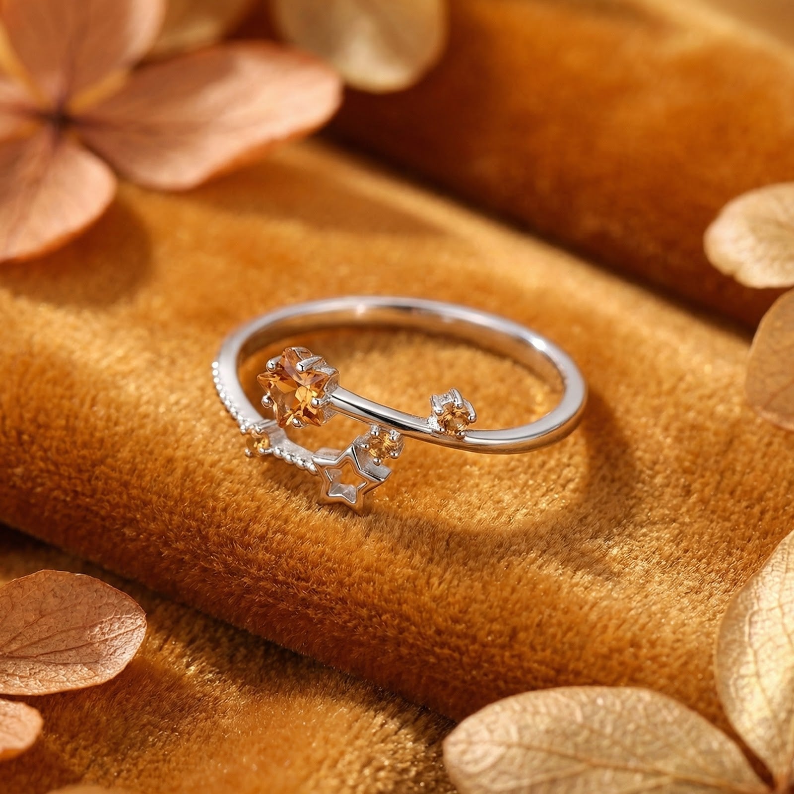 Sterling silver Astralis Star ring with golden simulated topaz stones on a warm velvet surface with autumn leaves.