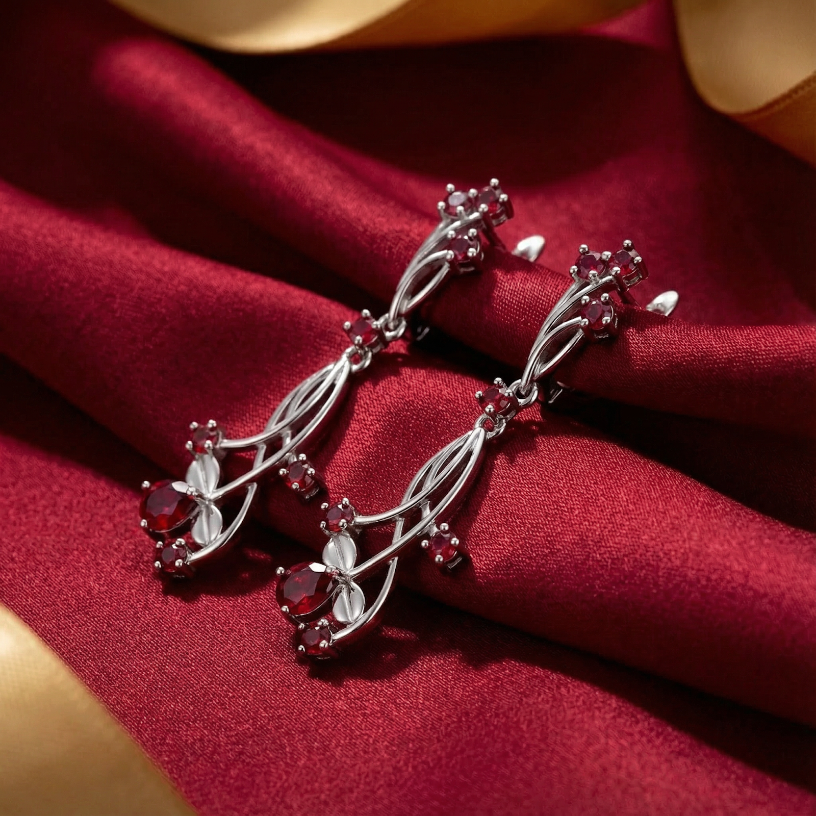 Side view of sterling silver drop earrings featuring vibrant red simulated rubies on textured red fabric.