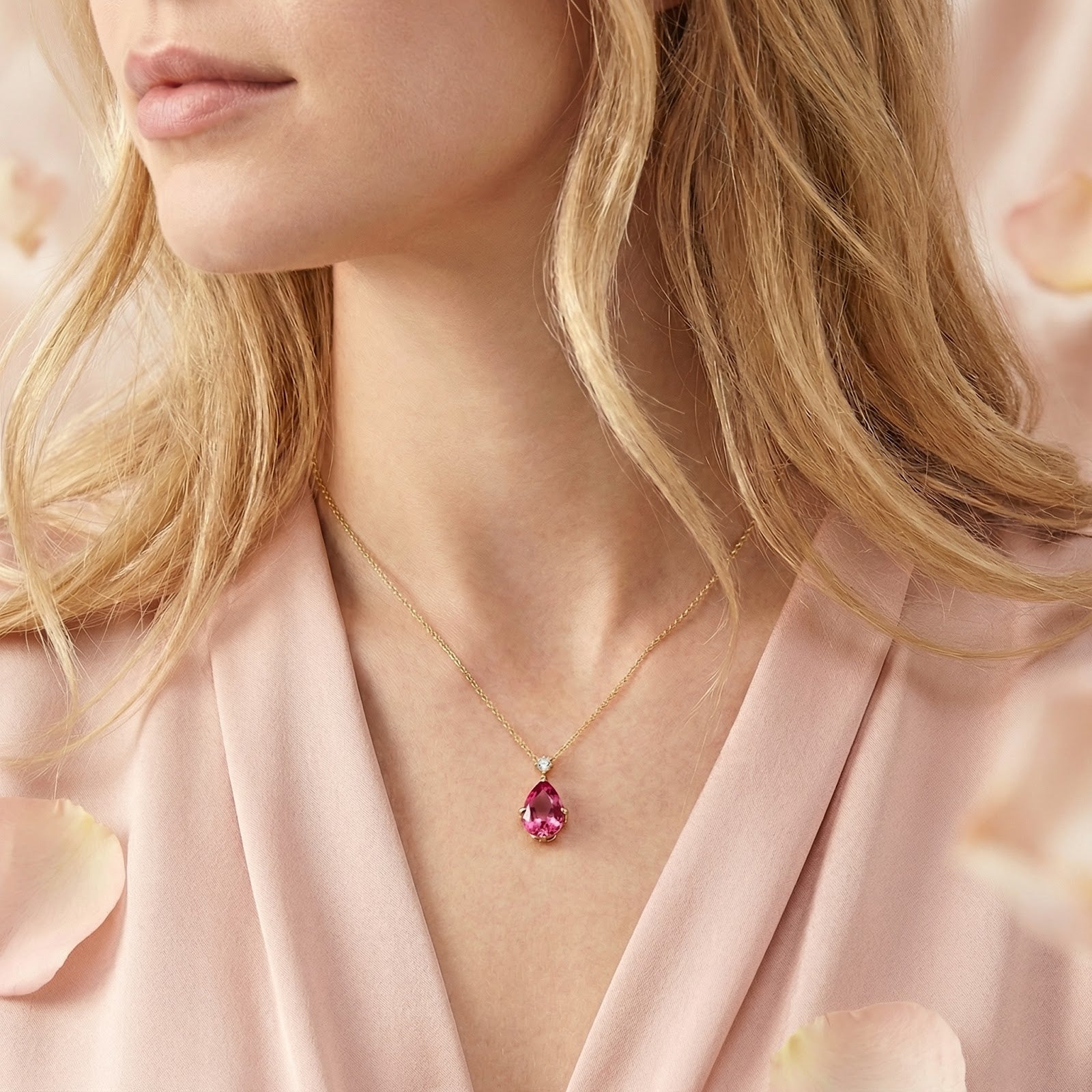 Woman wearing the pear-cut simulated pink tourmaline necklace in 18K gold vermeil over a pink V-neck top.