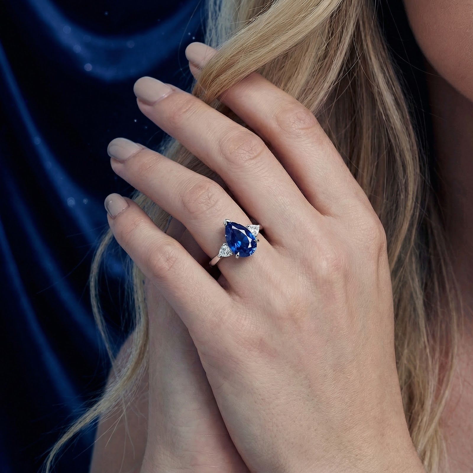 Pear-cut blue sapphire ring in sterling silver worn on a model's hand against a dark background.