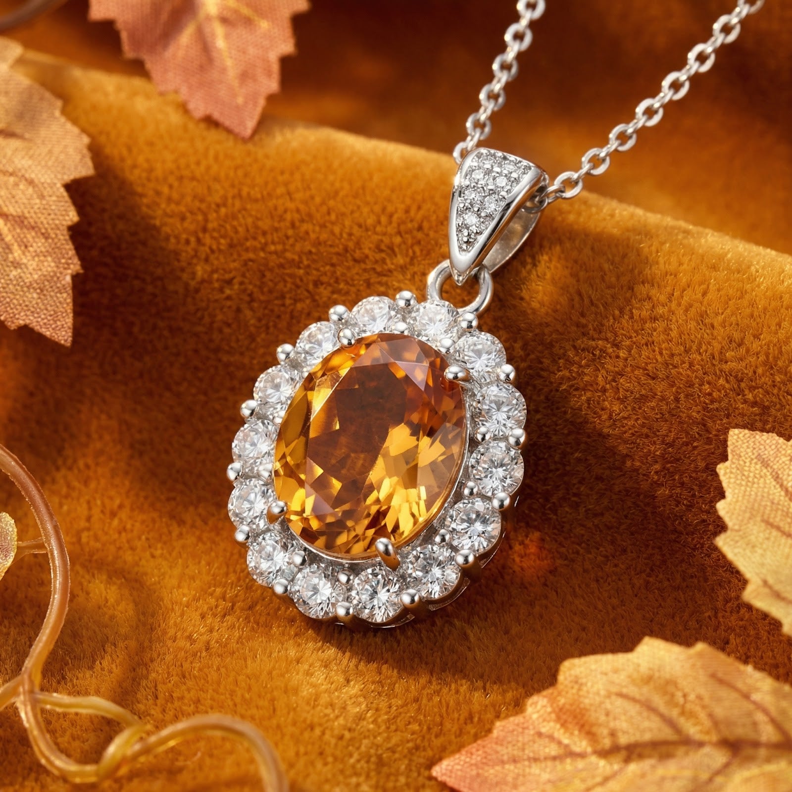 Oval-cut honeyed topaz halo necklace in sterling silver on an autumn-themed velvet background.