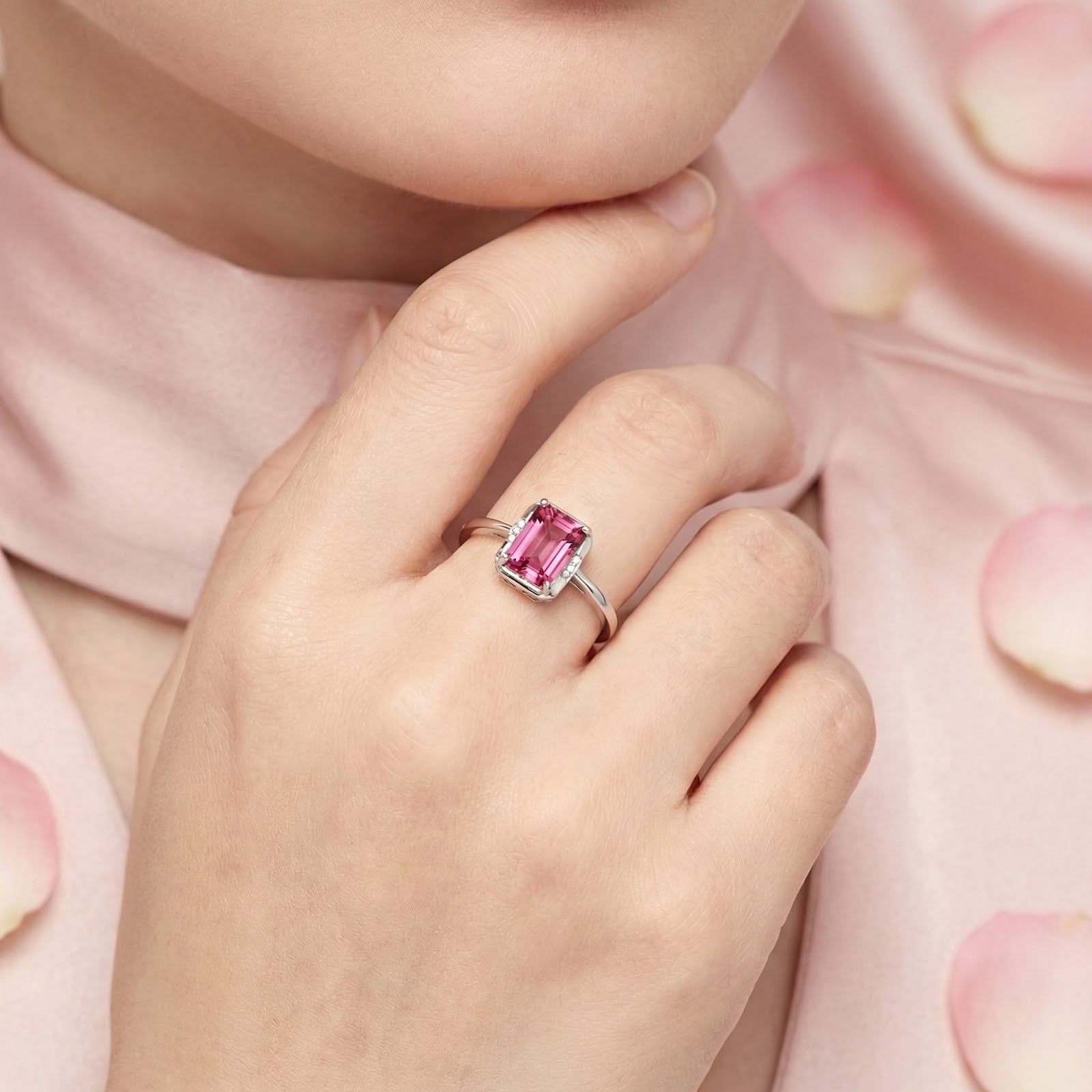 Woman wearing the emerald-cut pink tourmaline sterling silver ring on her finger against a pink background.