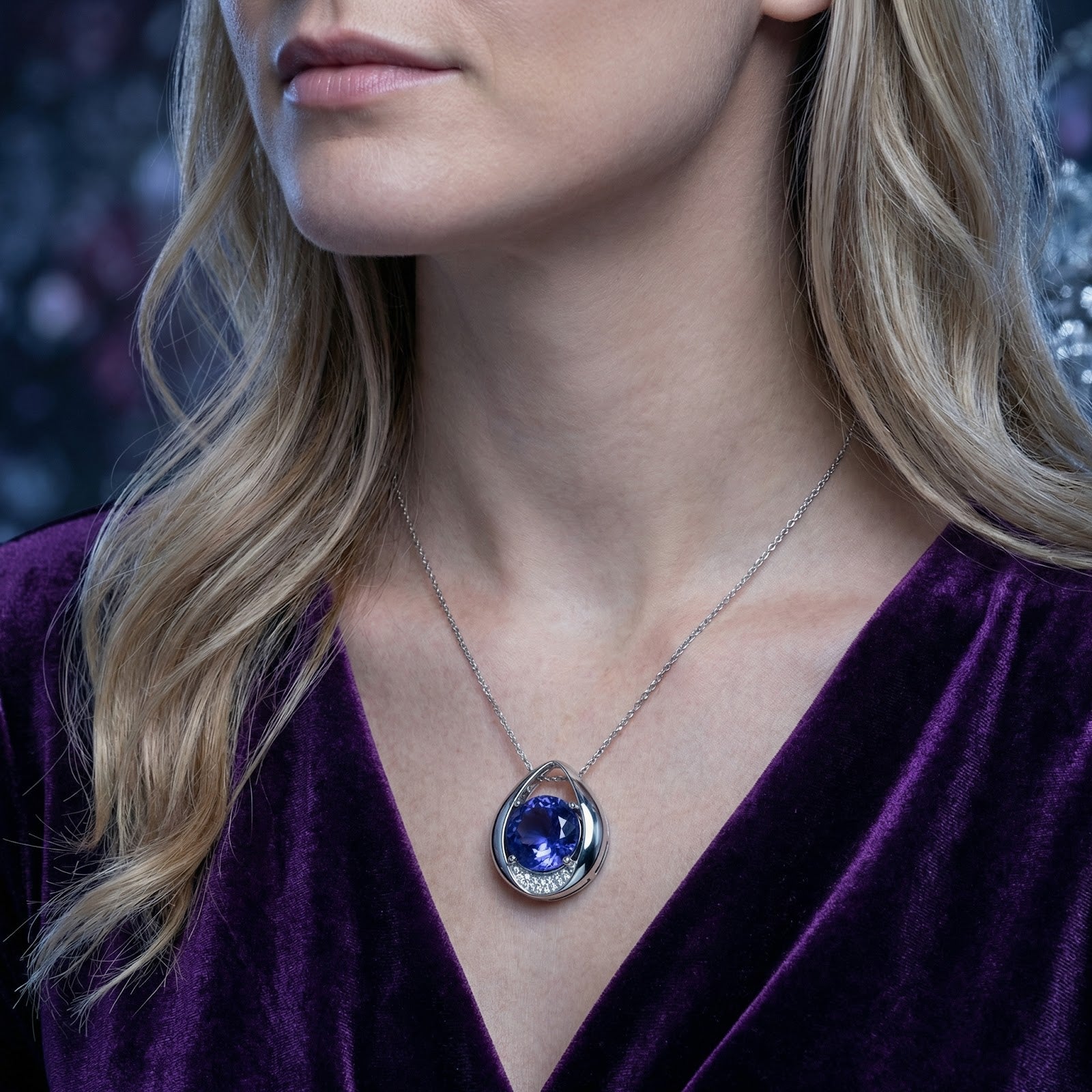 Model wearing the Elenara teardrop sterling silver necklace with a blue simulated tanzanite and purple velvet dress.