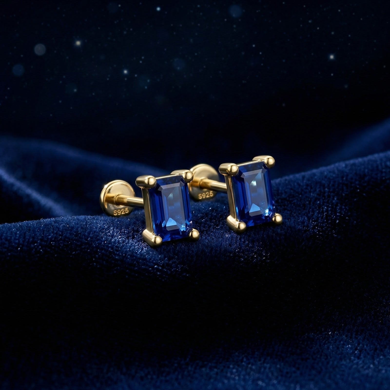 Baguette-cut blue simulated sapphire stud earrings in 18K gold vermeil on a dark blue velvet background.