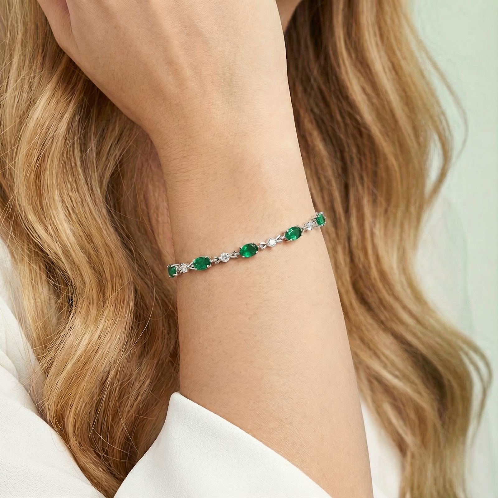 Sterling silver tennis bracelet with oval-cut simulated emeralds worn on a woman's wrist.