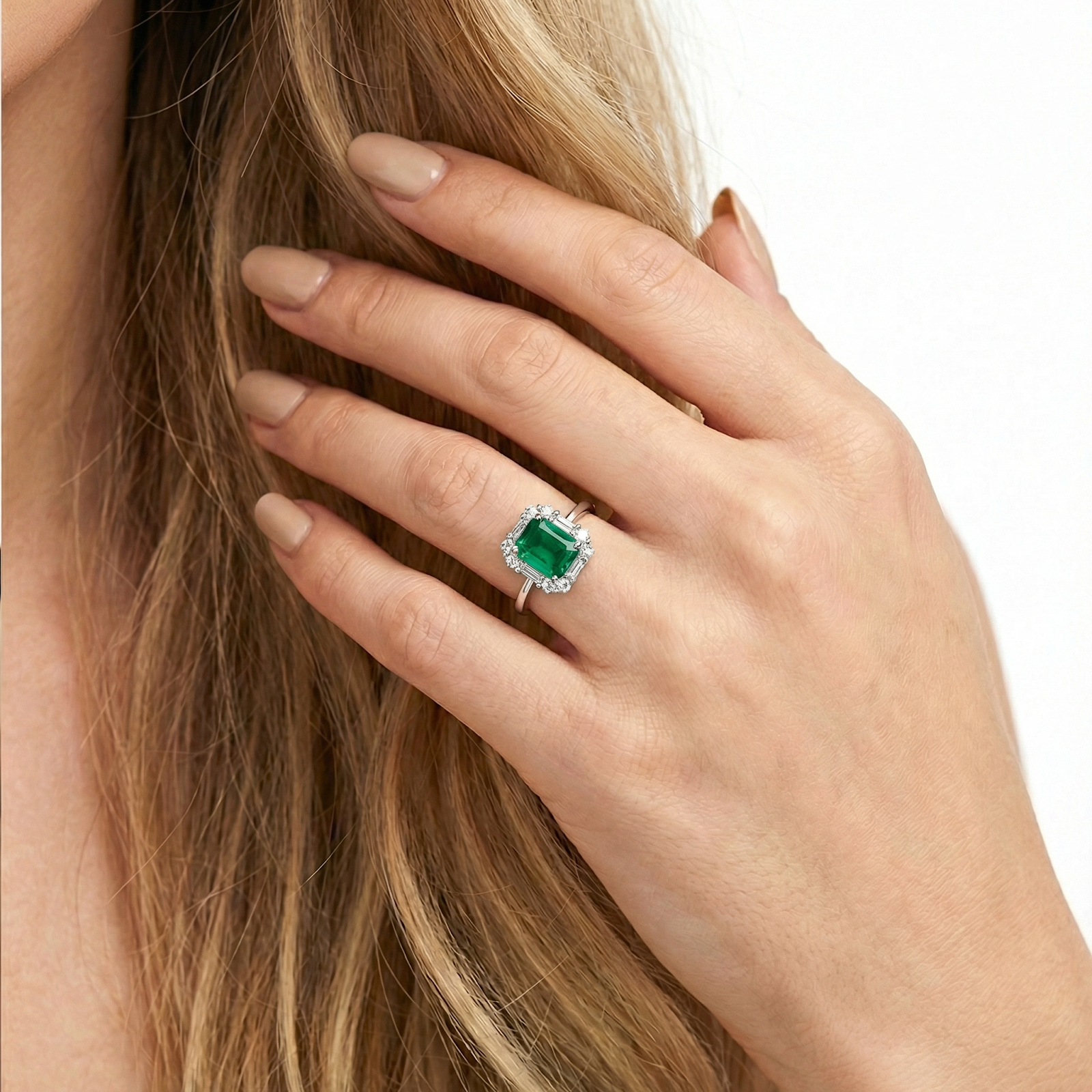 Close-up of a hand wearing the silver octagon simulated emerald ring with a halo of stones, touching blonde hair.