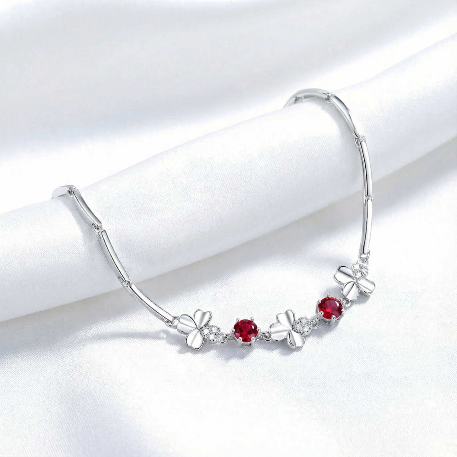 Silver clover bracelet with round-cut red simulated rubies draped over white silk.
