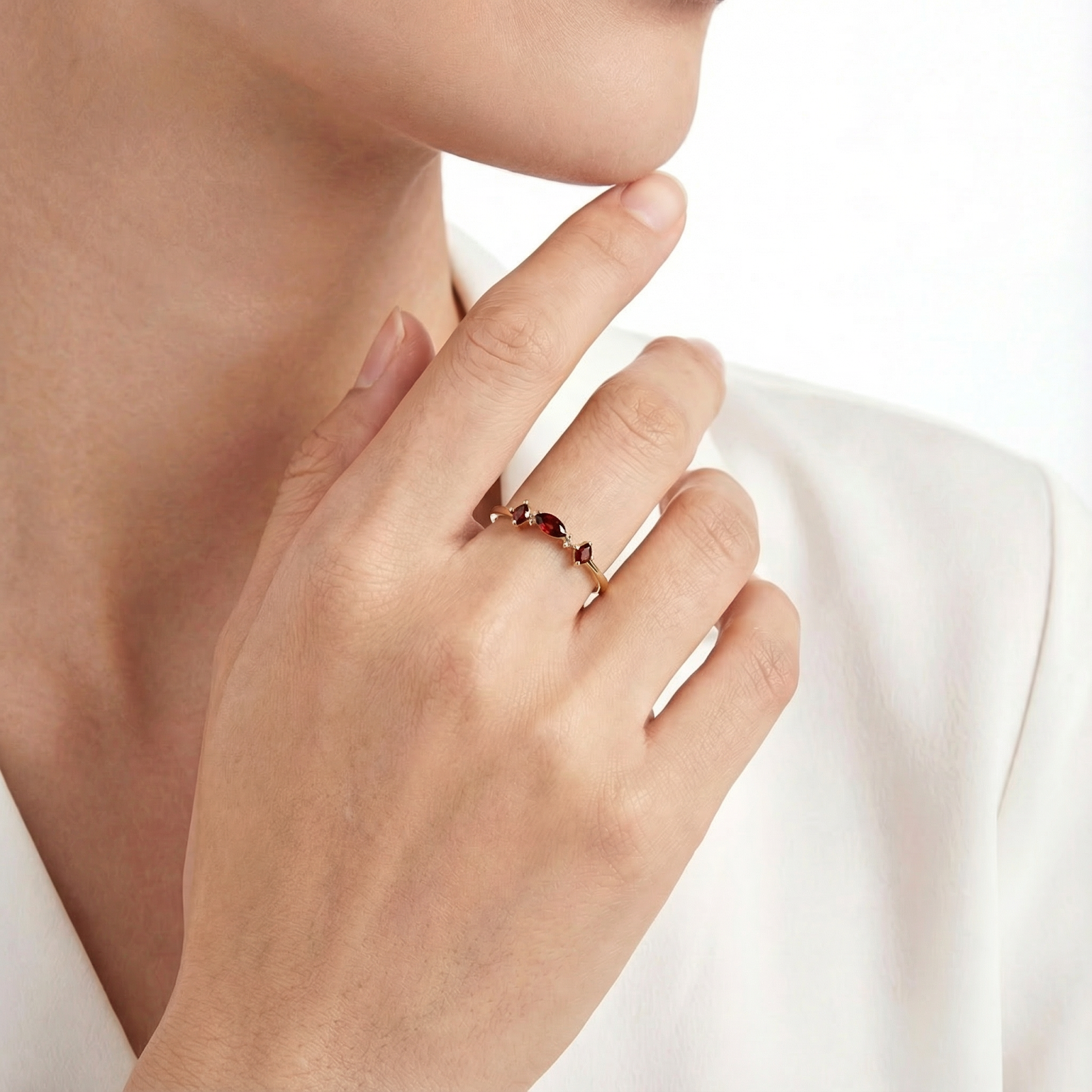 18K gold vermeil Lunette ring with red simulated garnet stones worn on a model's hand against a white outfit.