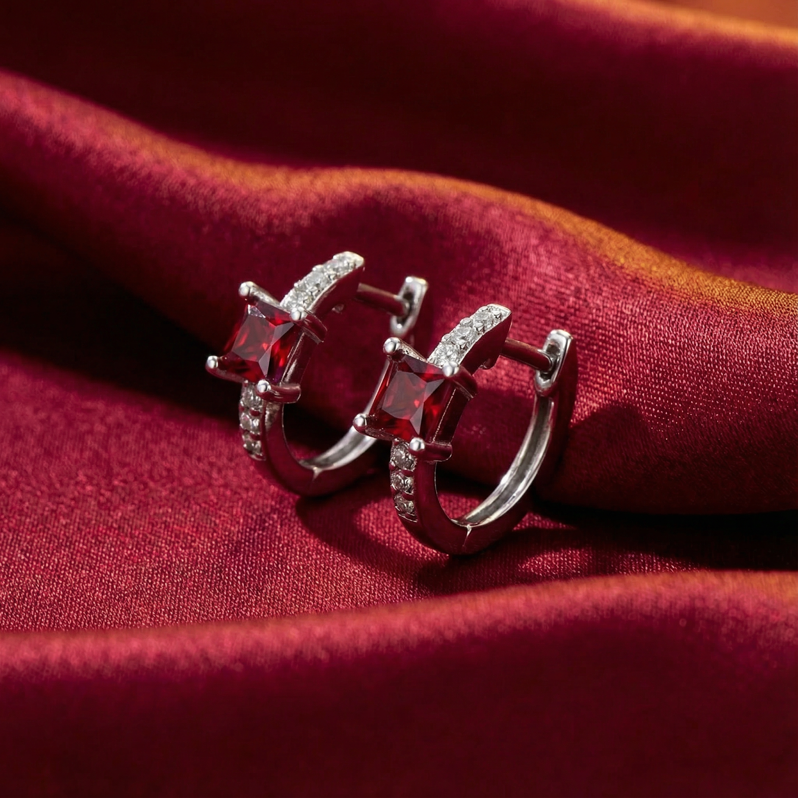Side view of sterling silver square huggies featuring princess-cut simulated rubies on red satin.