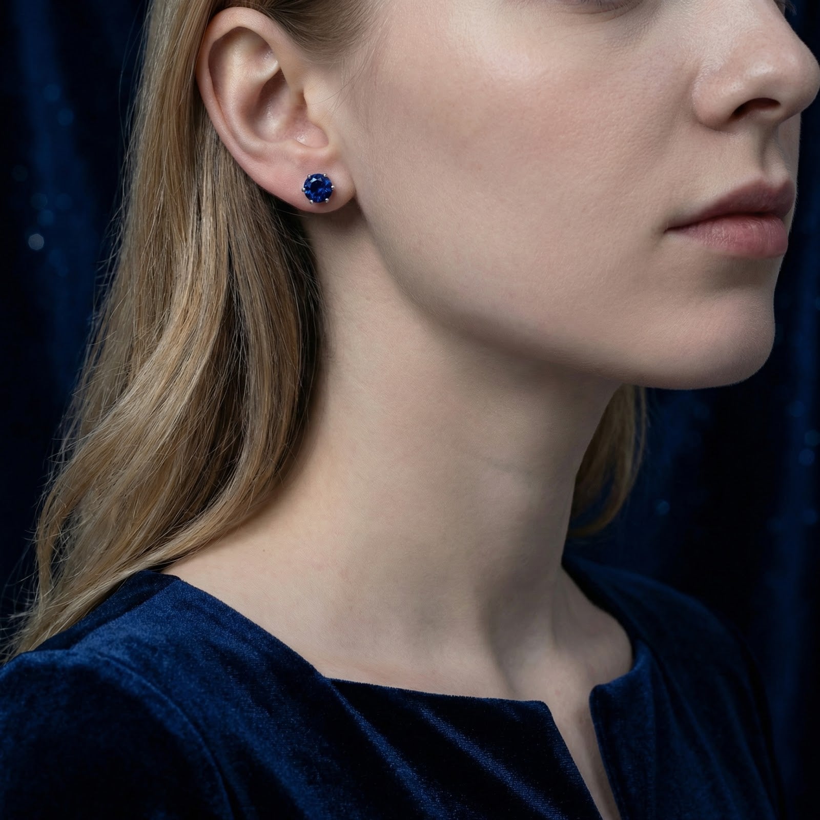 Woman wearing a round royal blue simulated sapphire stud earring in sterling silver.