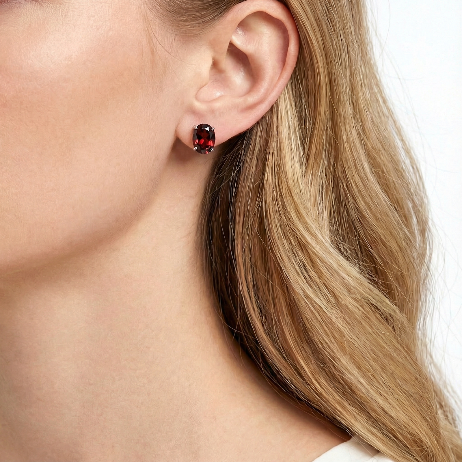 Close-up of a woman wearing the Aderyn oval cut simulated garnet earring in sterling silver on her ear.