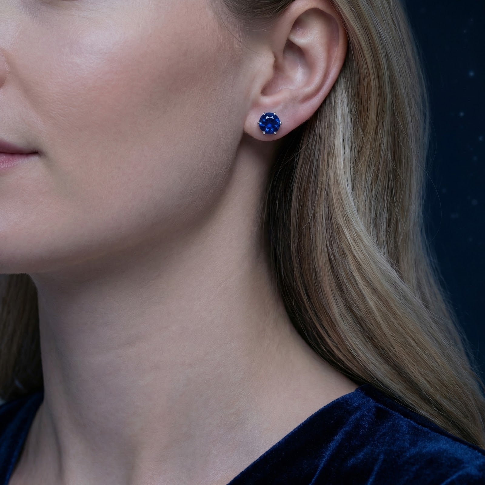 Side view of a woman wearing a round royal blue simulated sapphire stud earring in sterling silver.