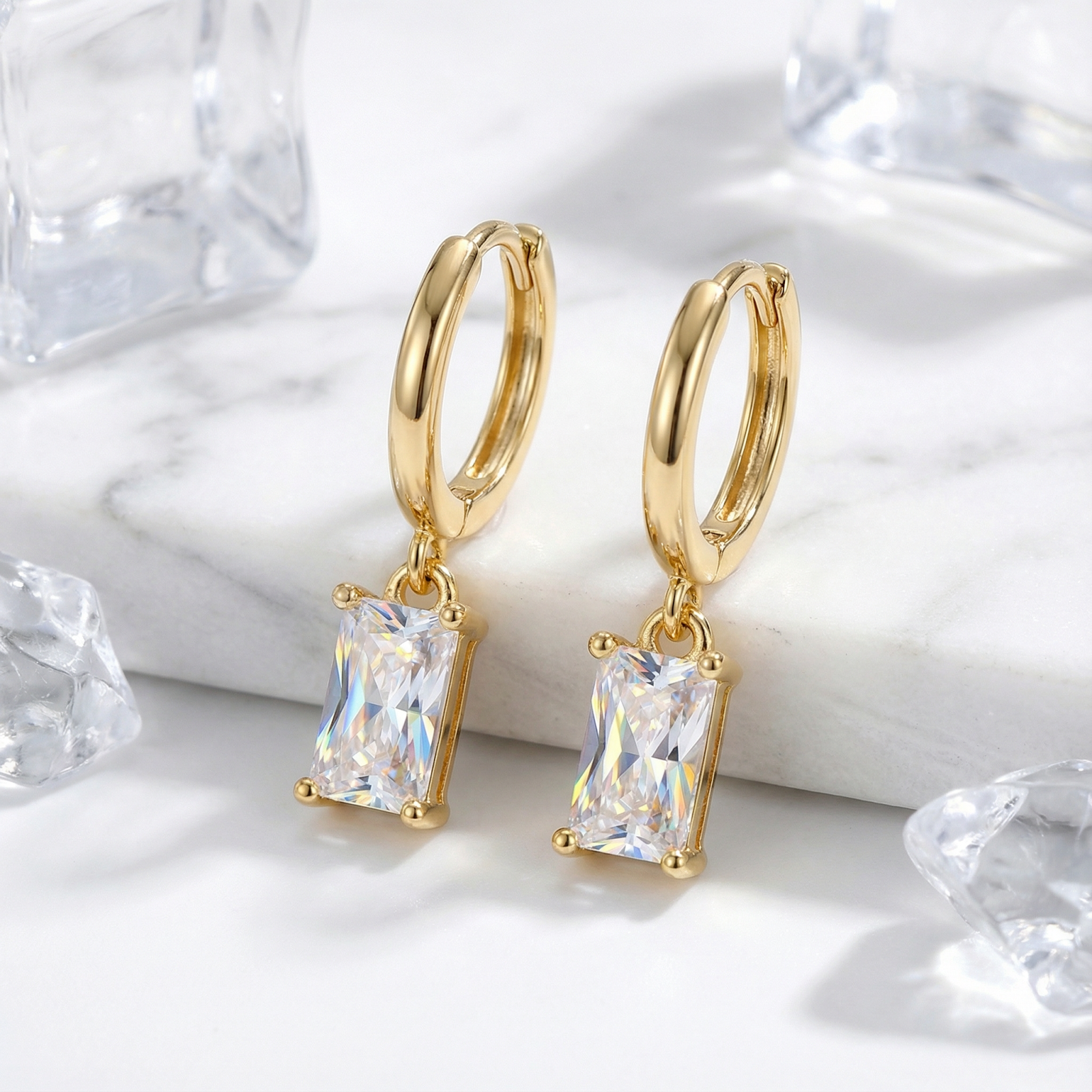 Close-up of 18K gold vermeil drop earrings featuring emerald cut simulated diamonds on marble.