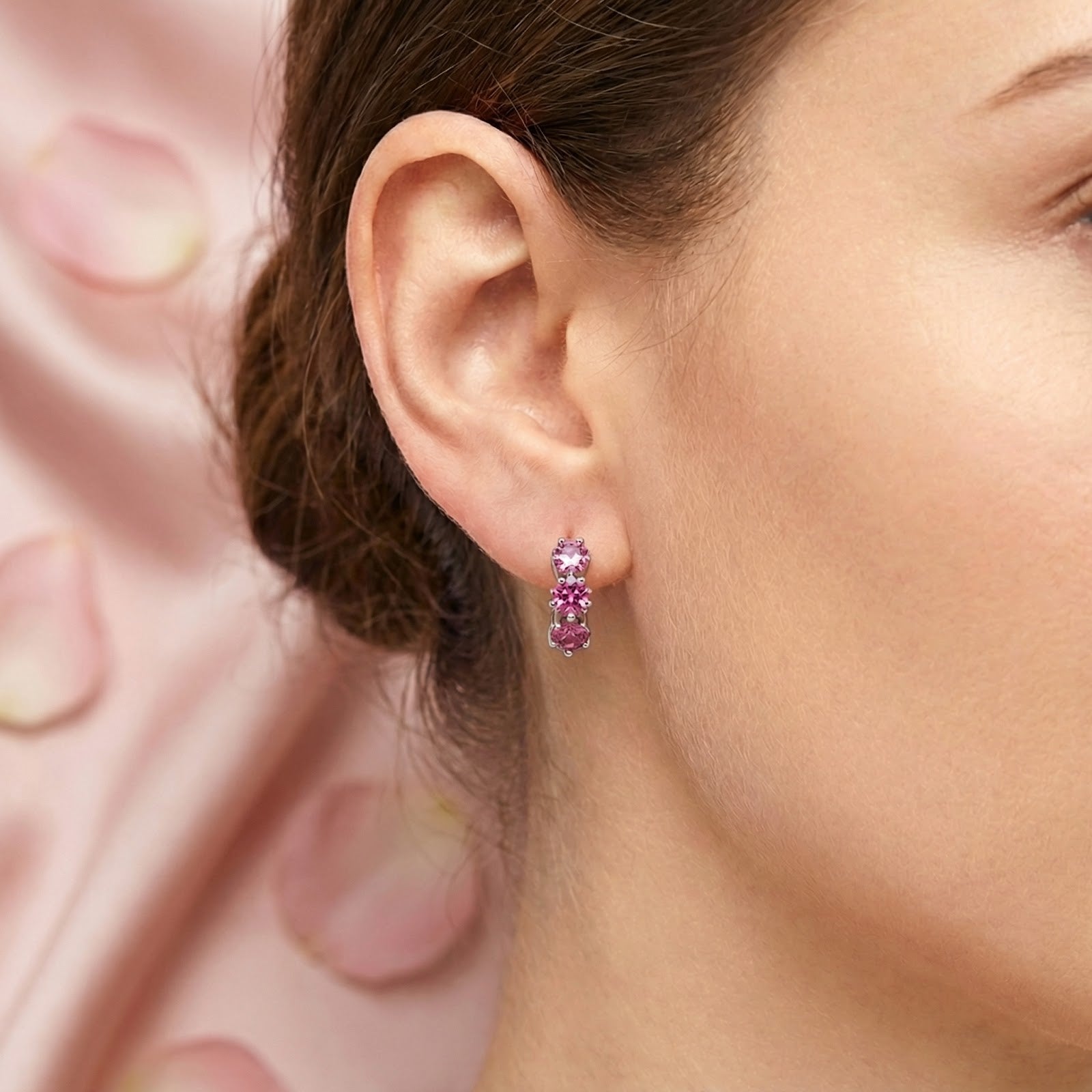 Close-up of a woman's ear wearing a sterling silver star huggie earring with three pink tourmaline stones.