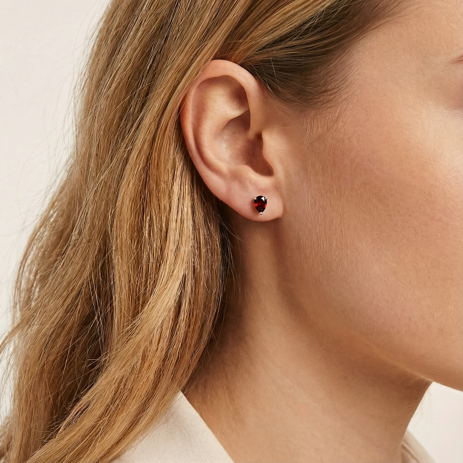 Woman wearing a pear cut simulated garnet stud earring in 18K gold vermeil on her earlobe.