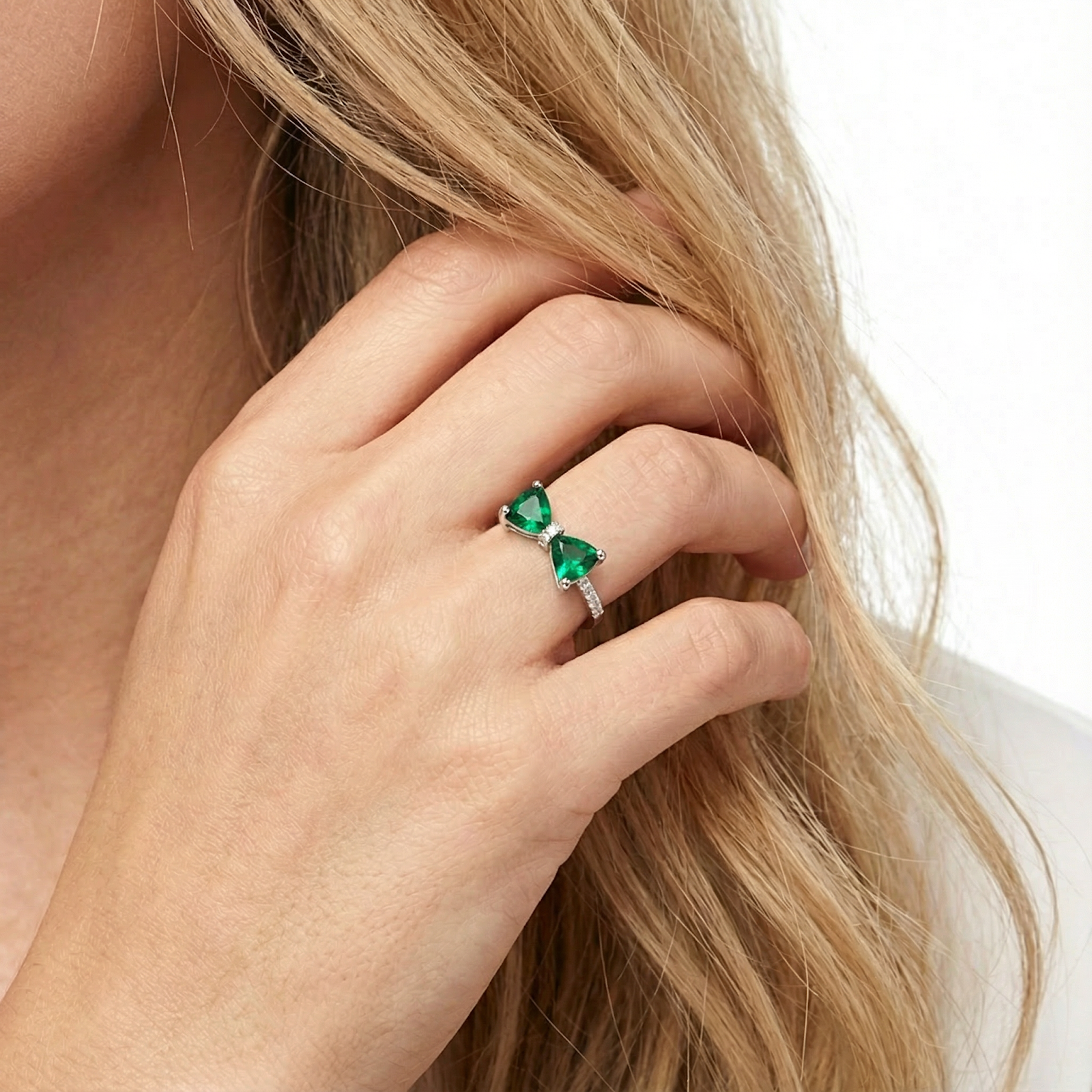 Woman wearing the sterling silver Alarise bow ring with trillion-cut simulated emeralds on her ring finger.