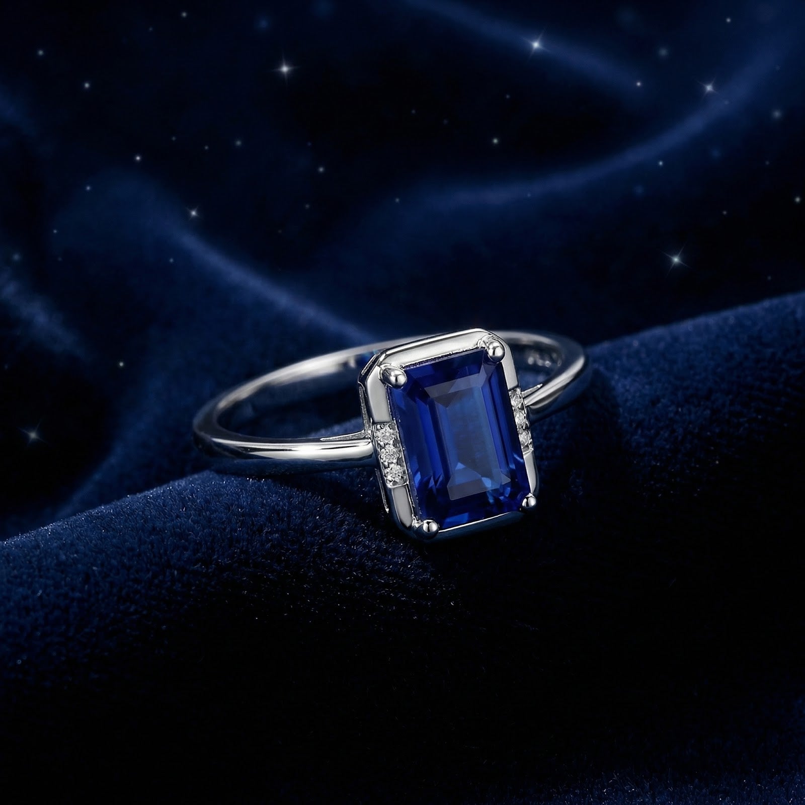 Emerald cut simulated sapphire ring in sterling silver on a dark blue velvet background with starry accents.