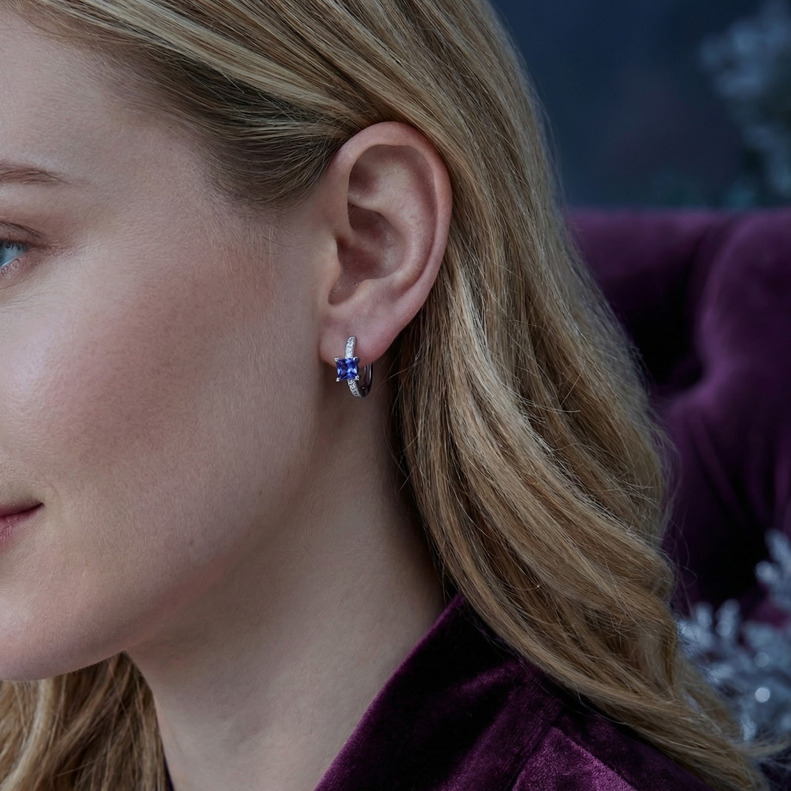 Woman wearing a sterling silver hoop earring with a square-cut simulated tanzanite stone.