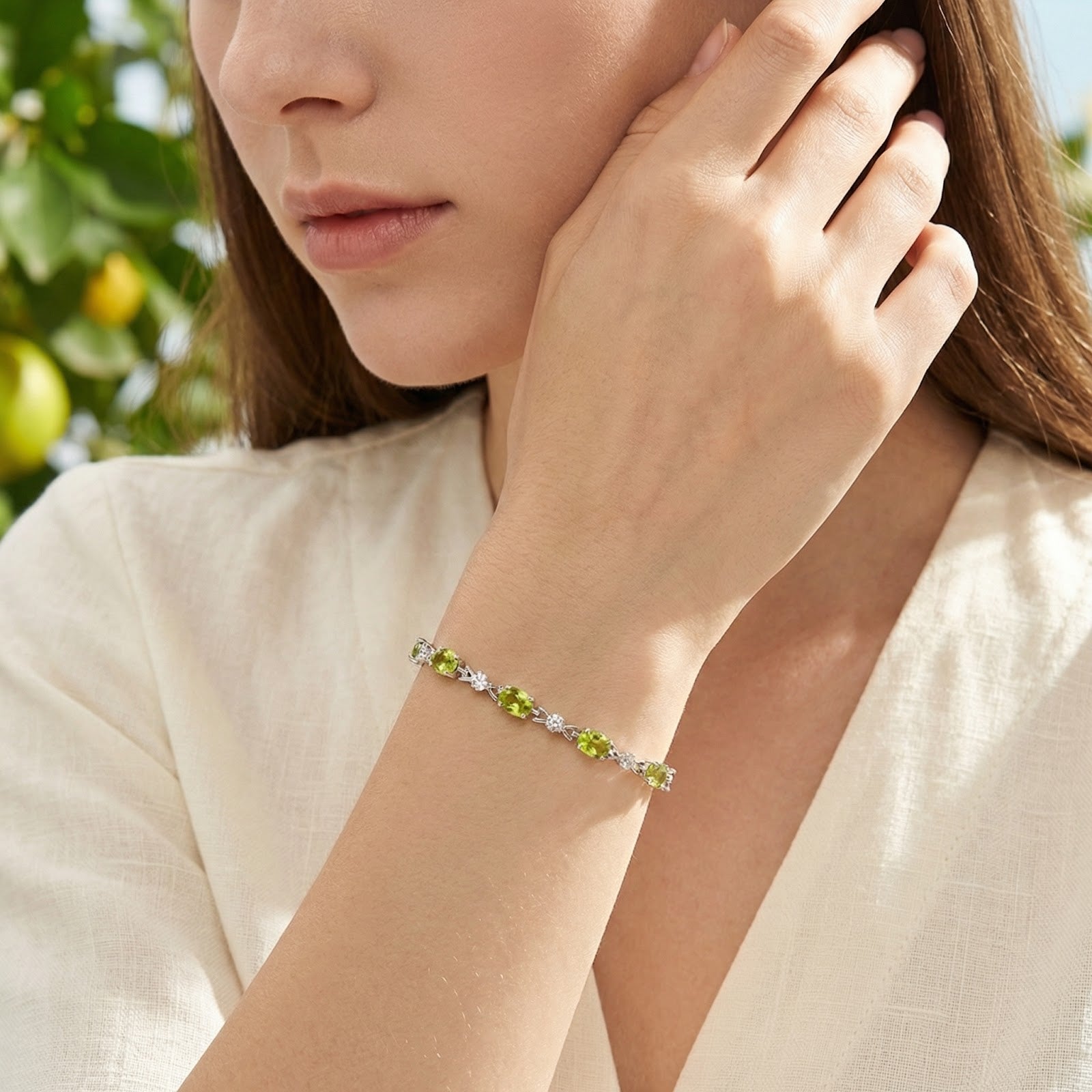 Simulated peridot tennis bracelet in sterling silver worn on a model's wrist in a lifestyle portrait setting.