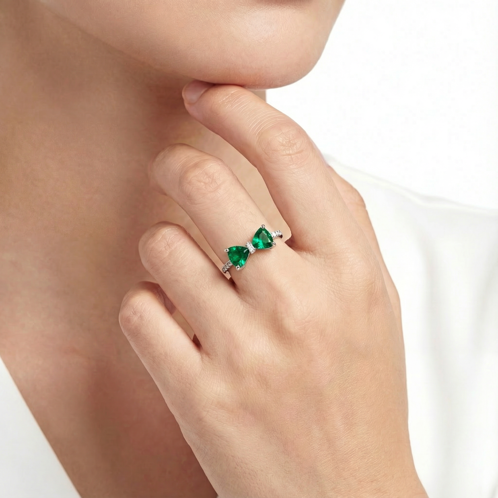 Sterling silver bow ring with green simulated emeralds worn on a woman's finger against a white background.
