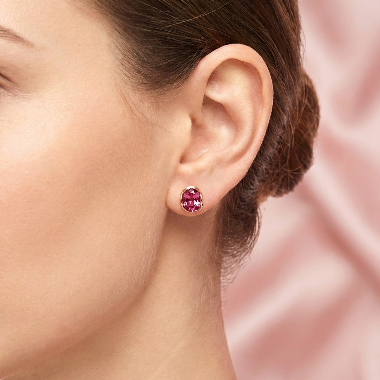 Woman wearing an 18K gold plated earring with a vivid oval pink tourmaline on her earlobe.