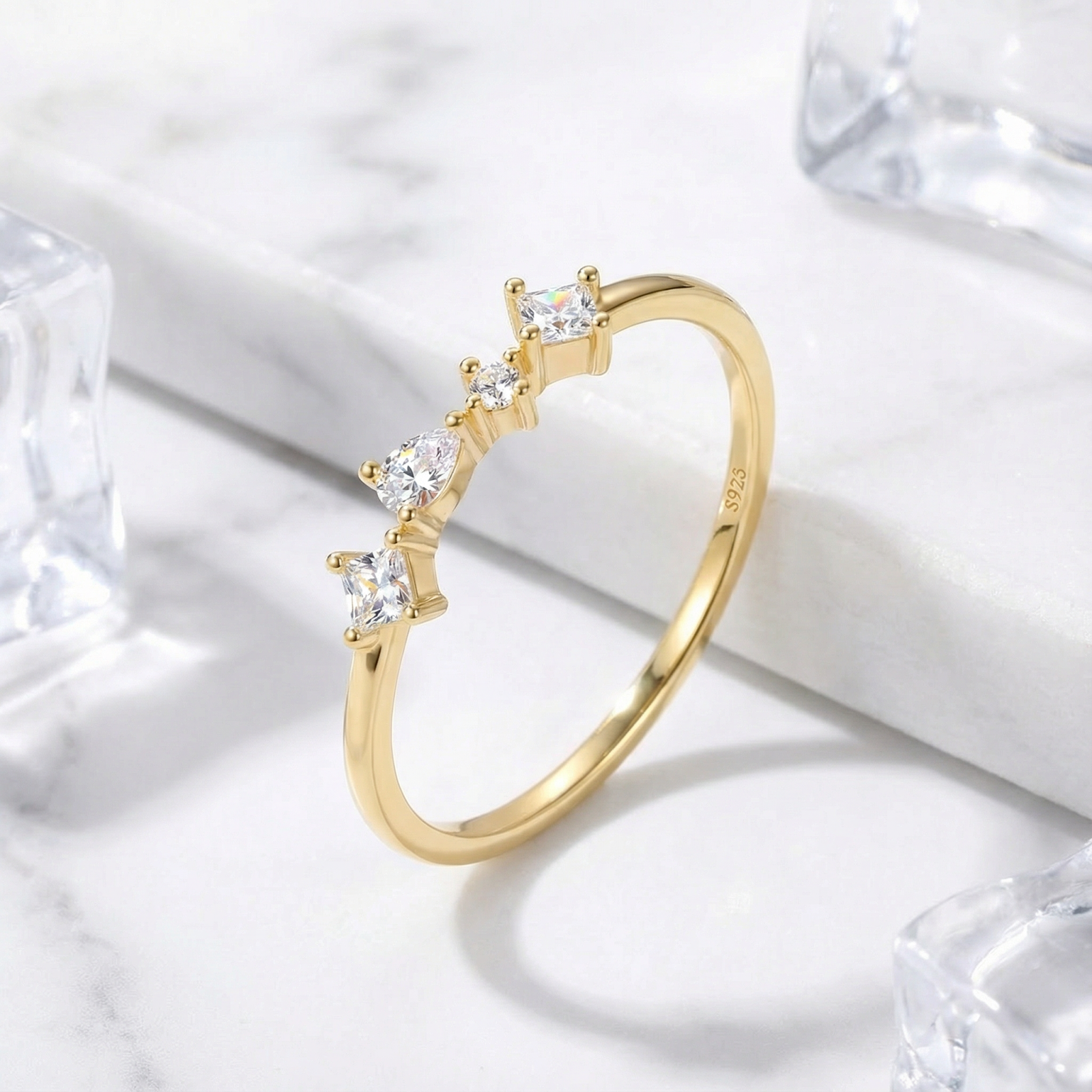 18K gold vermeil ring with graduated princess, pear, and round moissanite stones on marble with ice cubes.