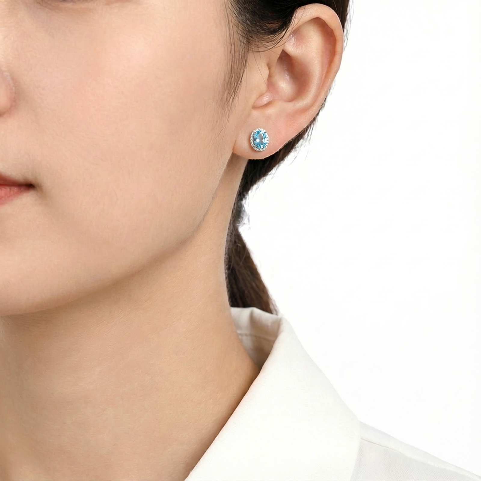 Model wearing an oval-cut simulated aquamarine halo stud earring in sterling silver on her ear.