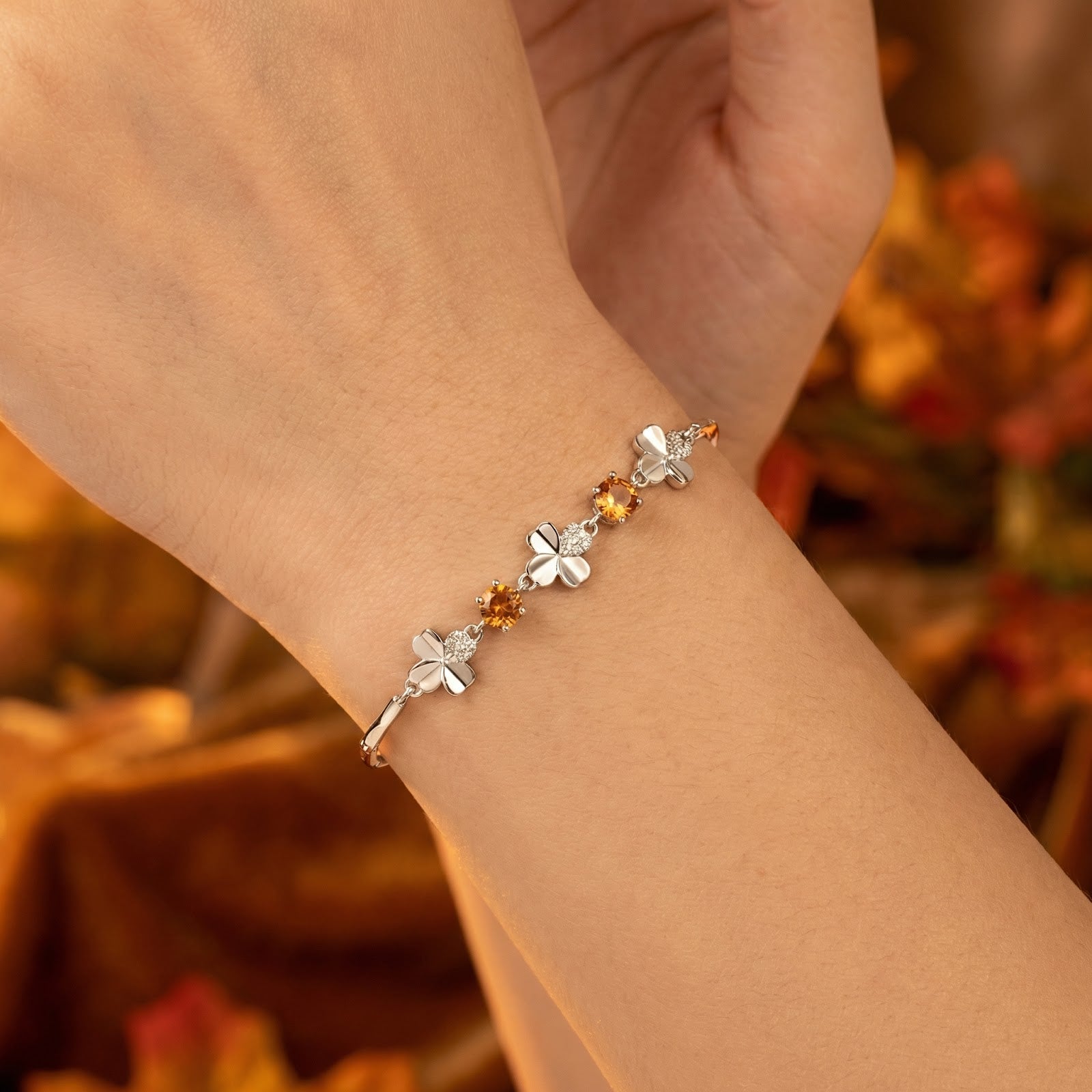 Close-up of the sterling silver clover bracelet with round honey simulated topaz stones worn on a woman's wrist.