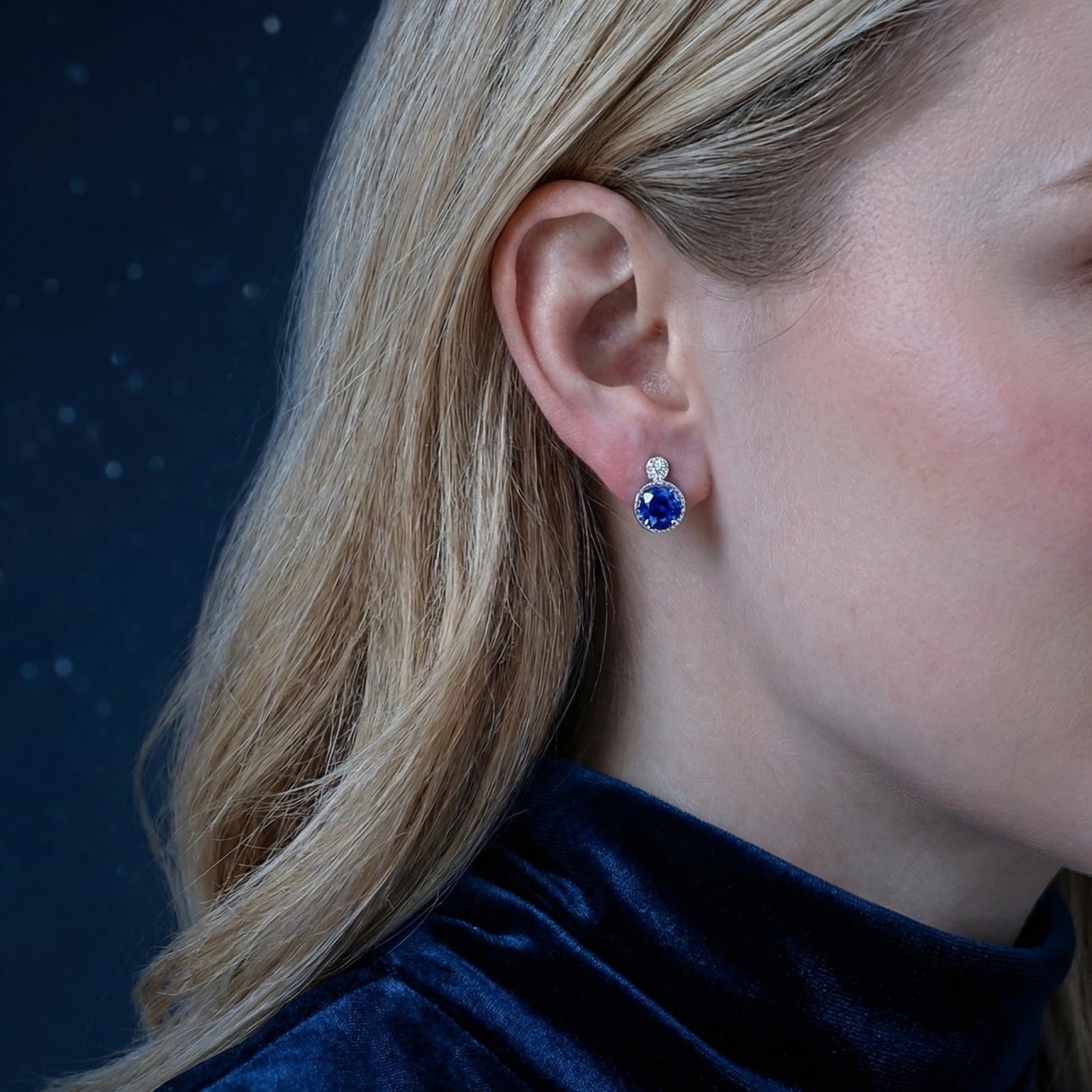 Blonde woman wearing a round blue simulated sapphire stud earring in S925 sterling silver.