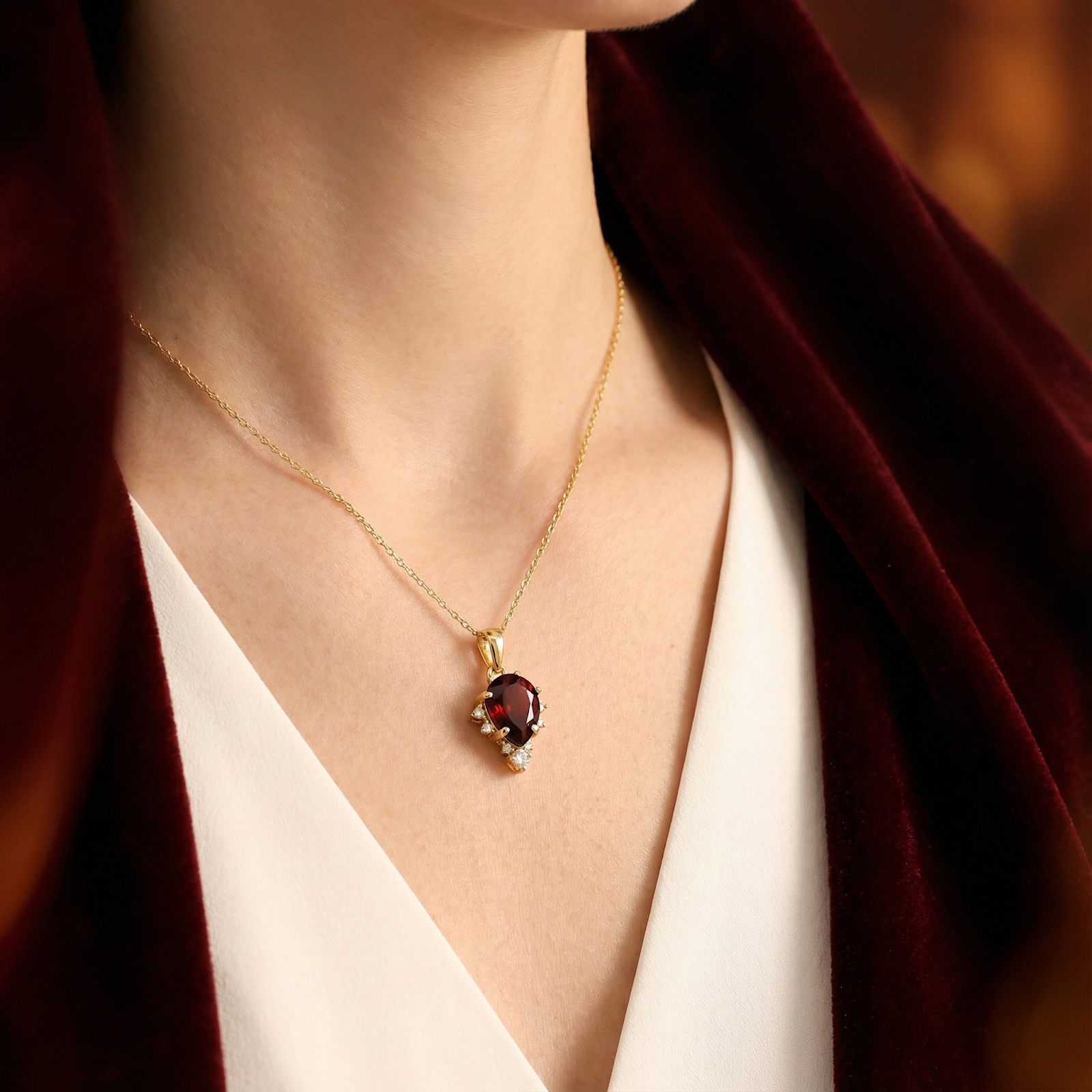 Model wearing the 18K gold vermeil teardrop garnet necklace paired with a luxurious red velvet wrap.