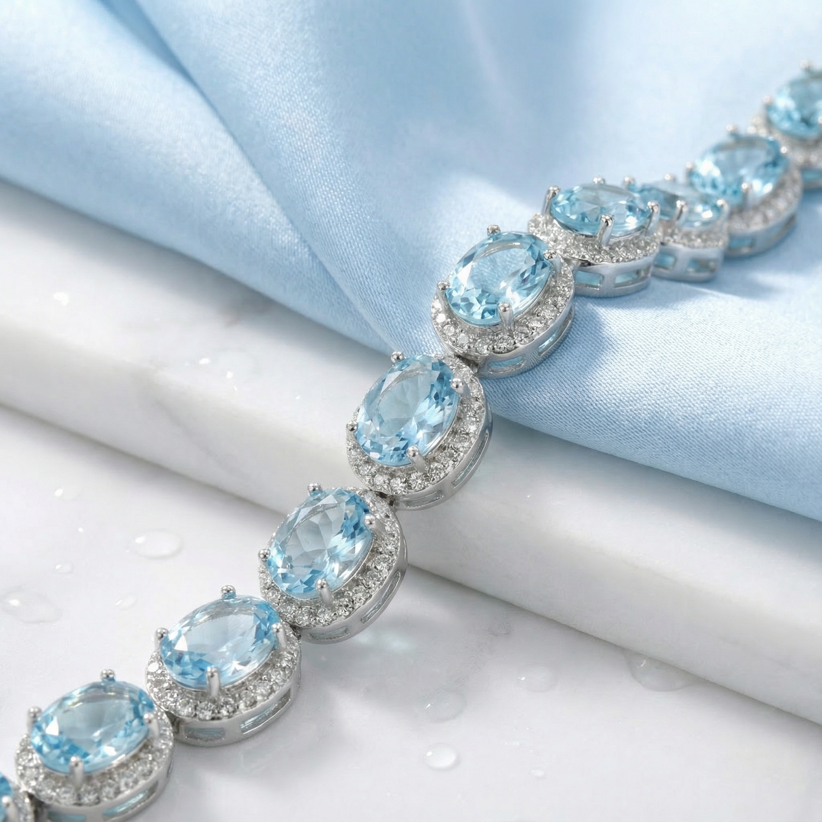 Close-up of oval simulated aquamarine stones and halo settings on a rhodium-plated sterling silver bracelet.