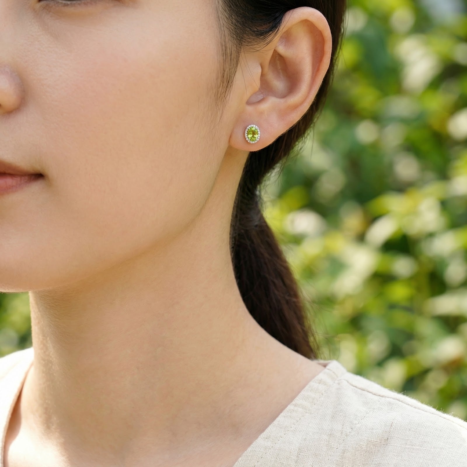 Woman wearing a Zelara oval peridot halo stud earring in sterling silver for a classic jewelry look.