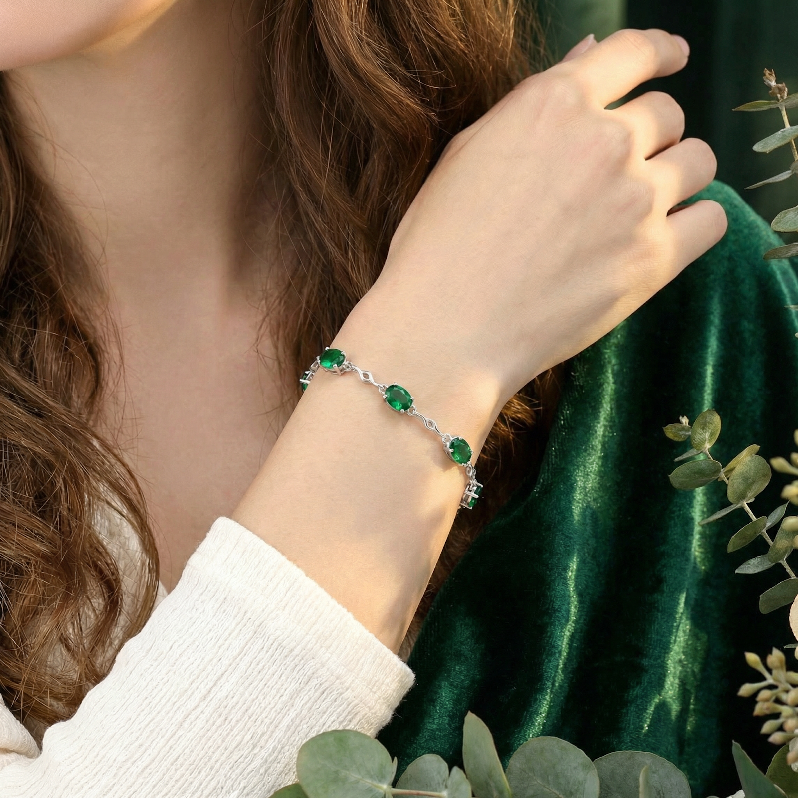 Woman's wrist featuring the silver simulated emerald station bracelet against a green velvet background.