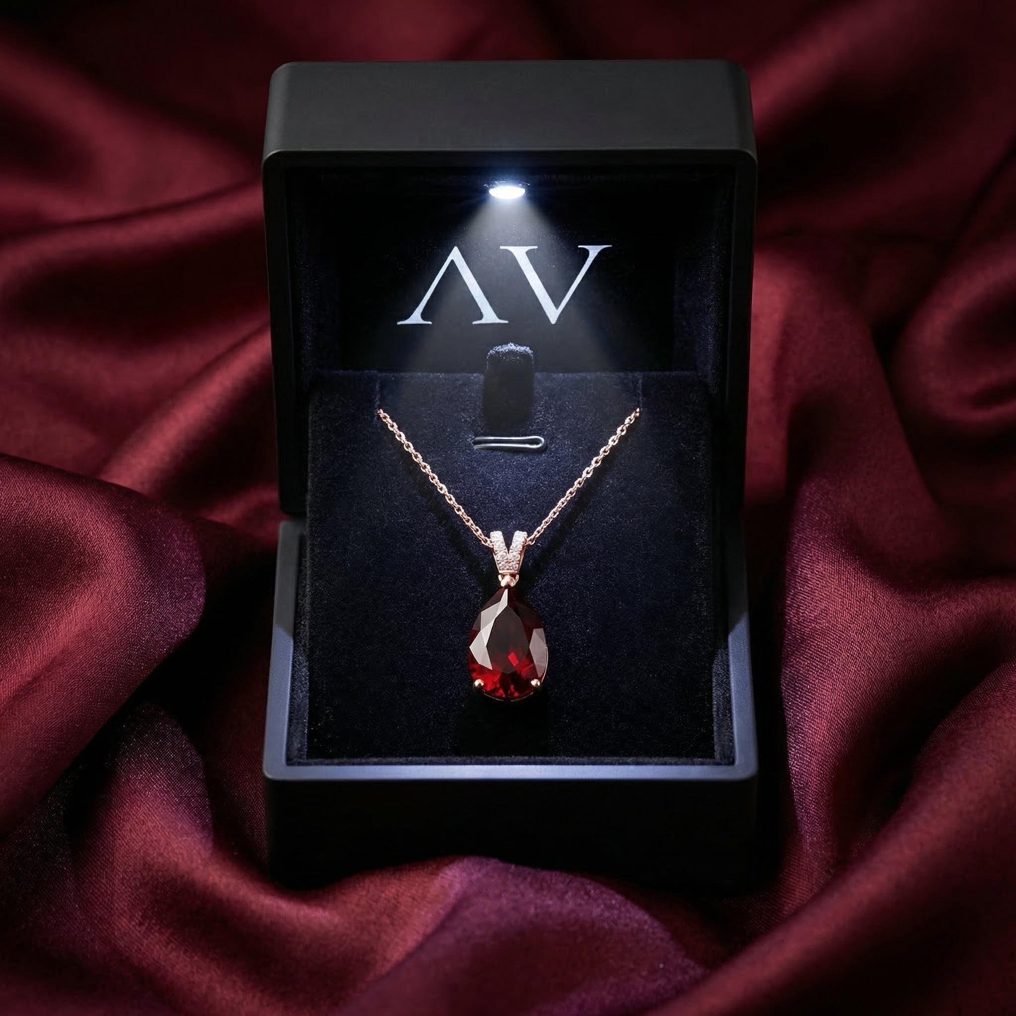 Pear cut garnet necklace in 18K rose gold presented in a lighted black jewelry box on burgundy silk.