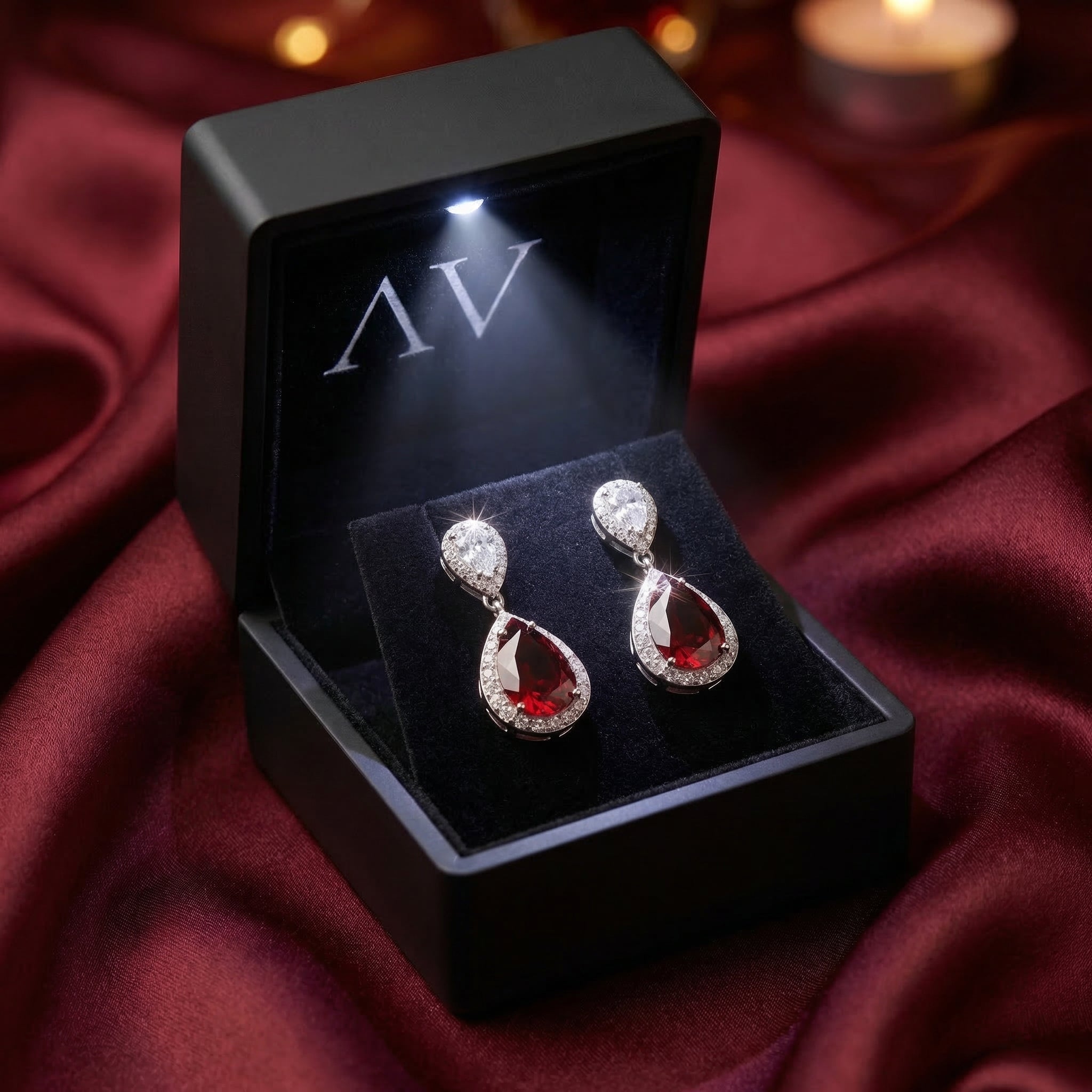 Rosaria red garnet drop earrings displayed in a black LED-lit jewelry box on burgundy fabric.
