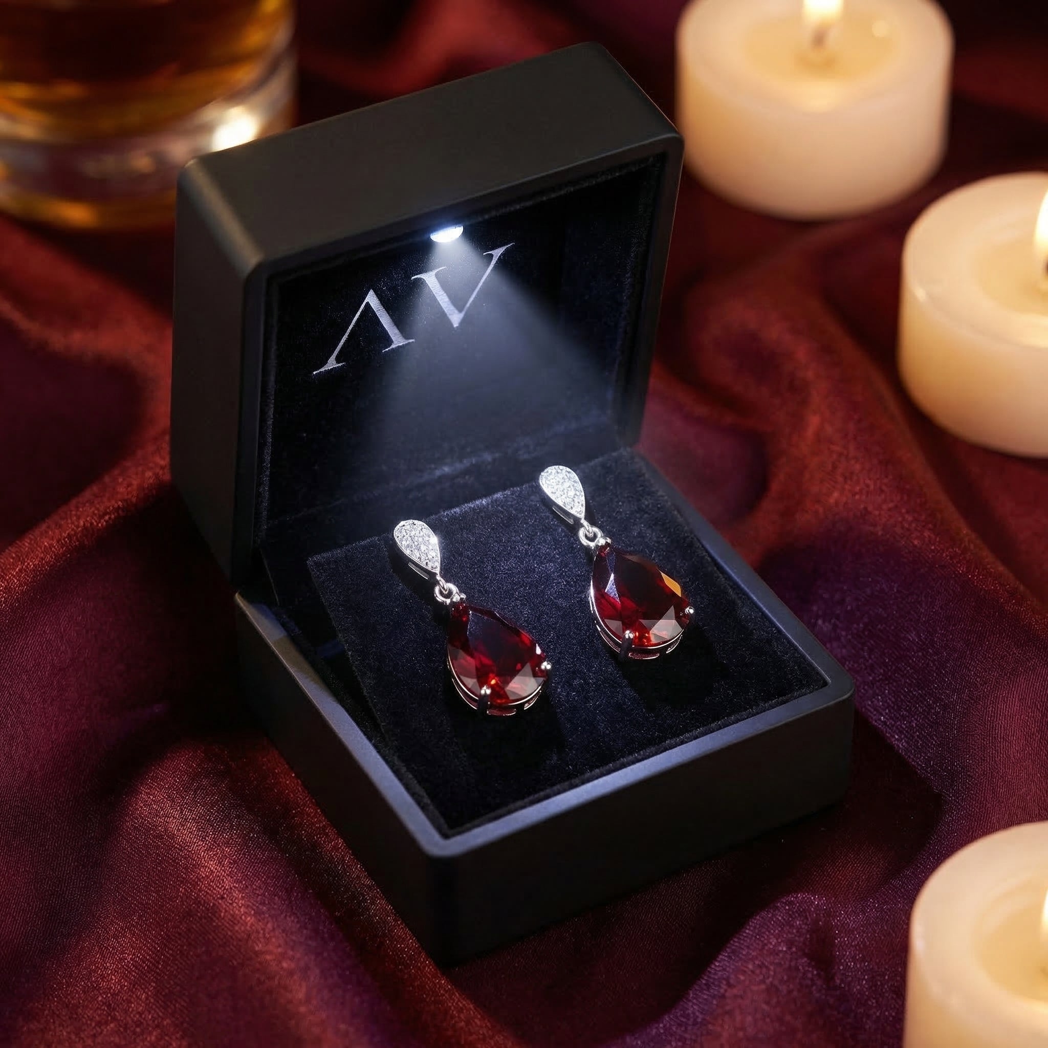 Sterling silver pear cut garnet earrings presented in a luxury black LED-lighted gift box on red silk fabric.