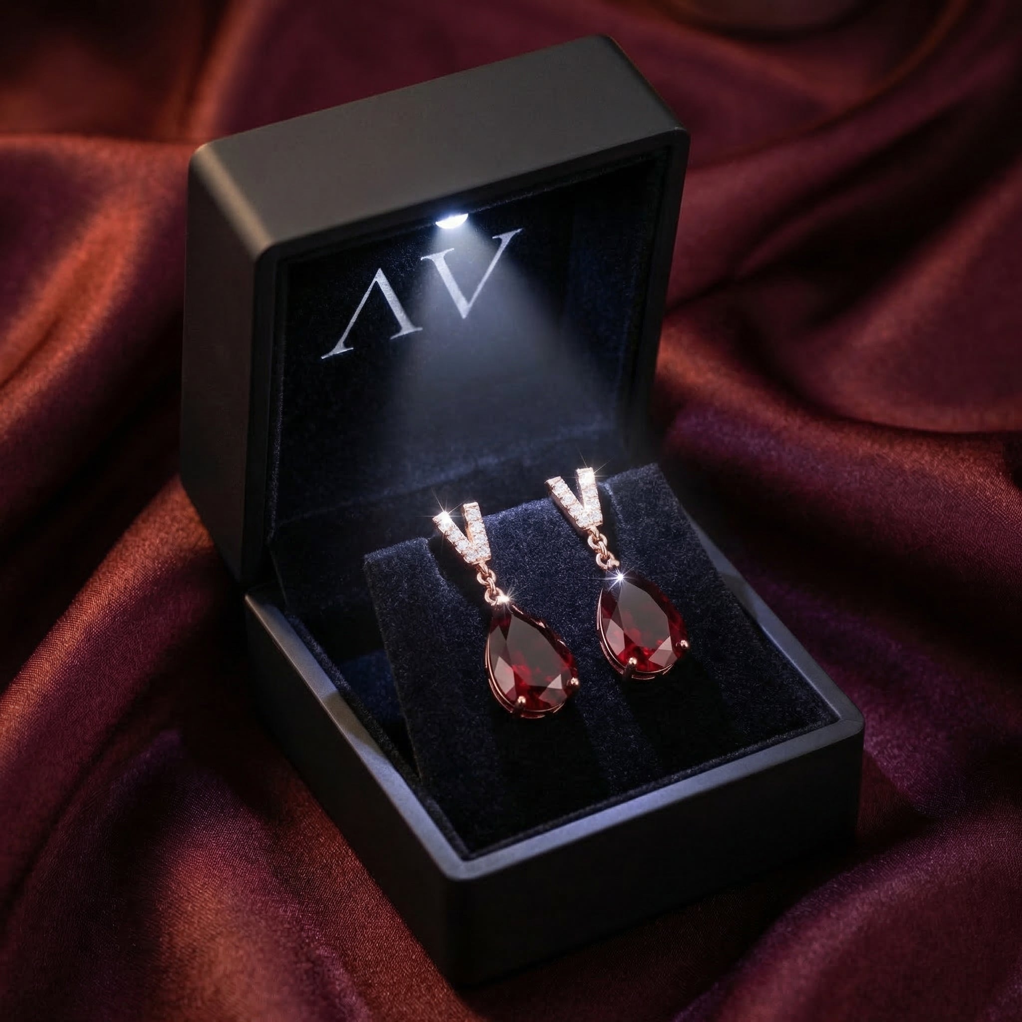 Olyndra pear earrings in 18K rose gold with pear-cut garnets inside a lighted black jewelry gift box.