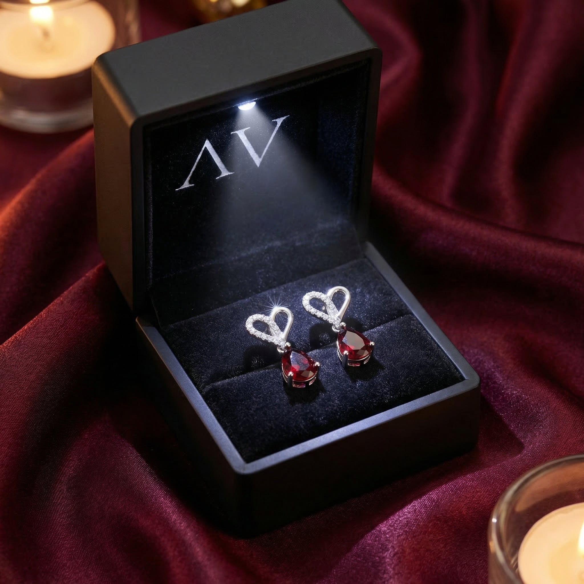 Lovisa garnet pear drop earrings in a black LED-lit presentation box on a dark red fabric background.