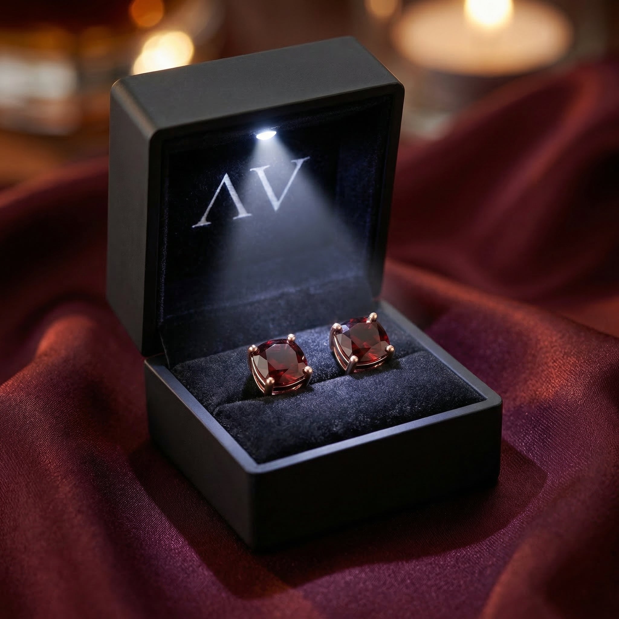 Cushion cut red garnet earrings in 18K rose gold presented in a black lighted jewelry box.