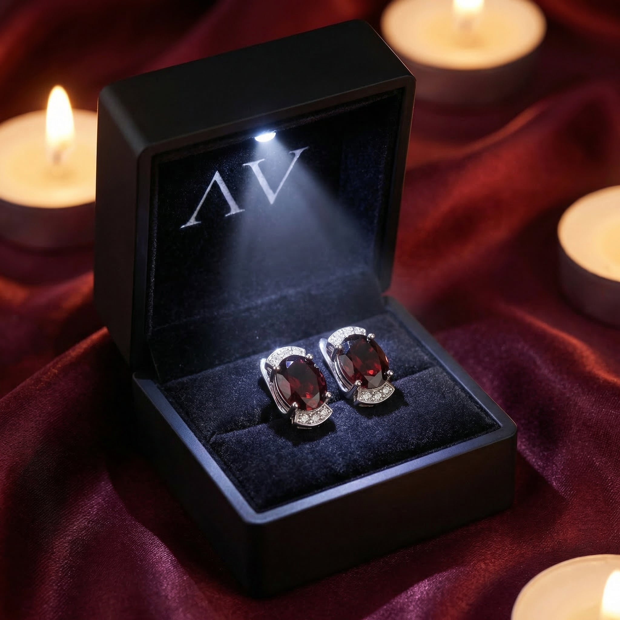 Oval natural garnet drop earrings presented in a black LED-lit gift box on red silk fabric with candles.
