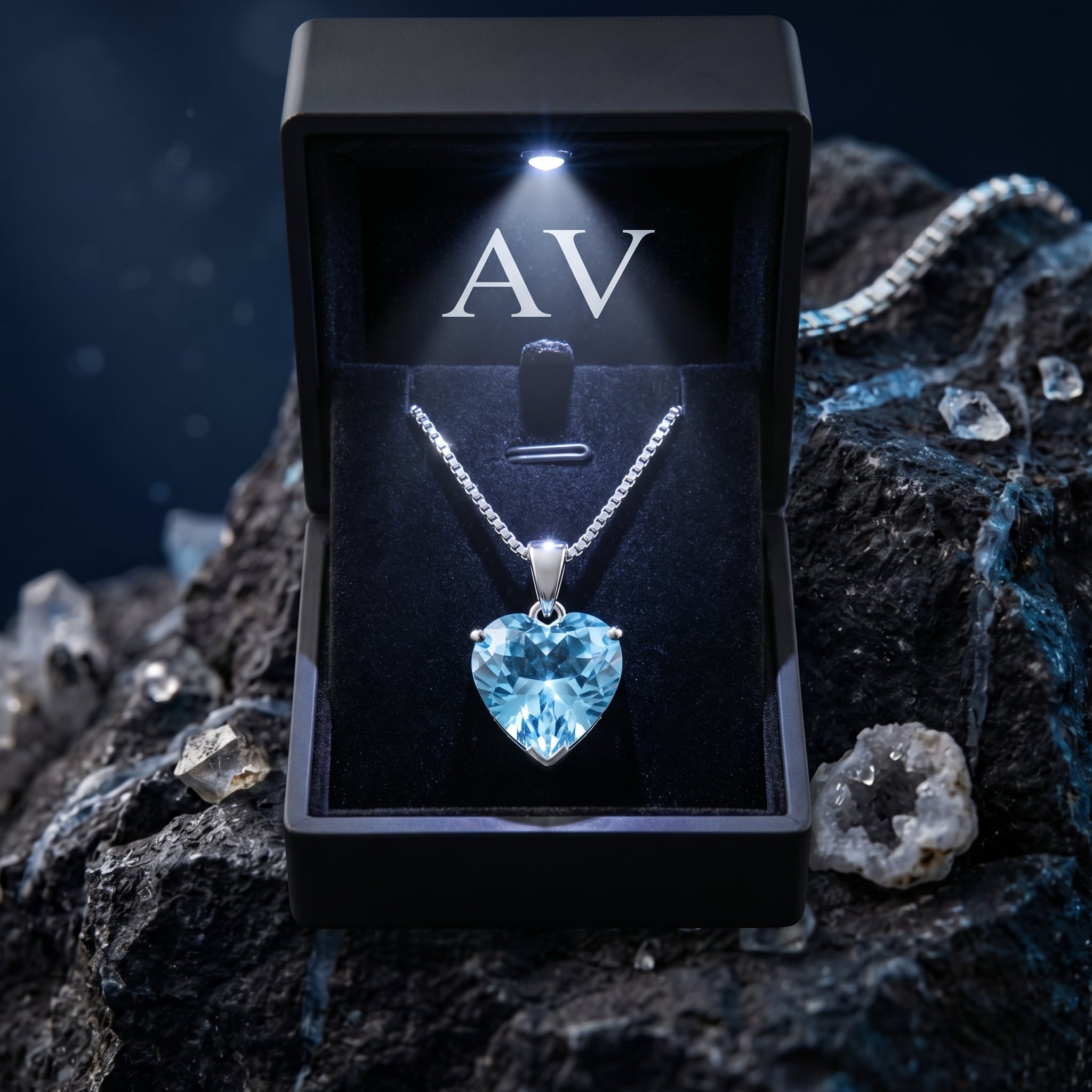 Heart-cut blue topaz necklace in a black lighted gift box, presented on a dark rocky background.