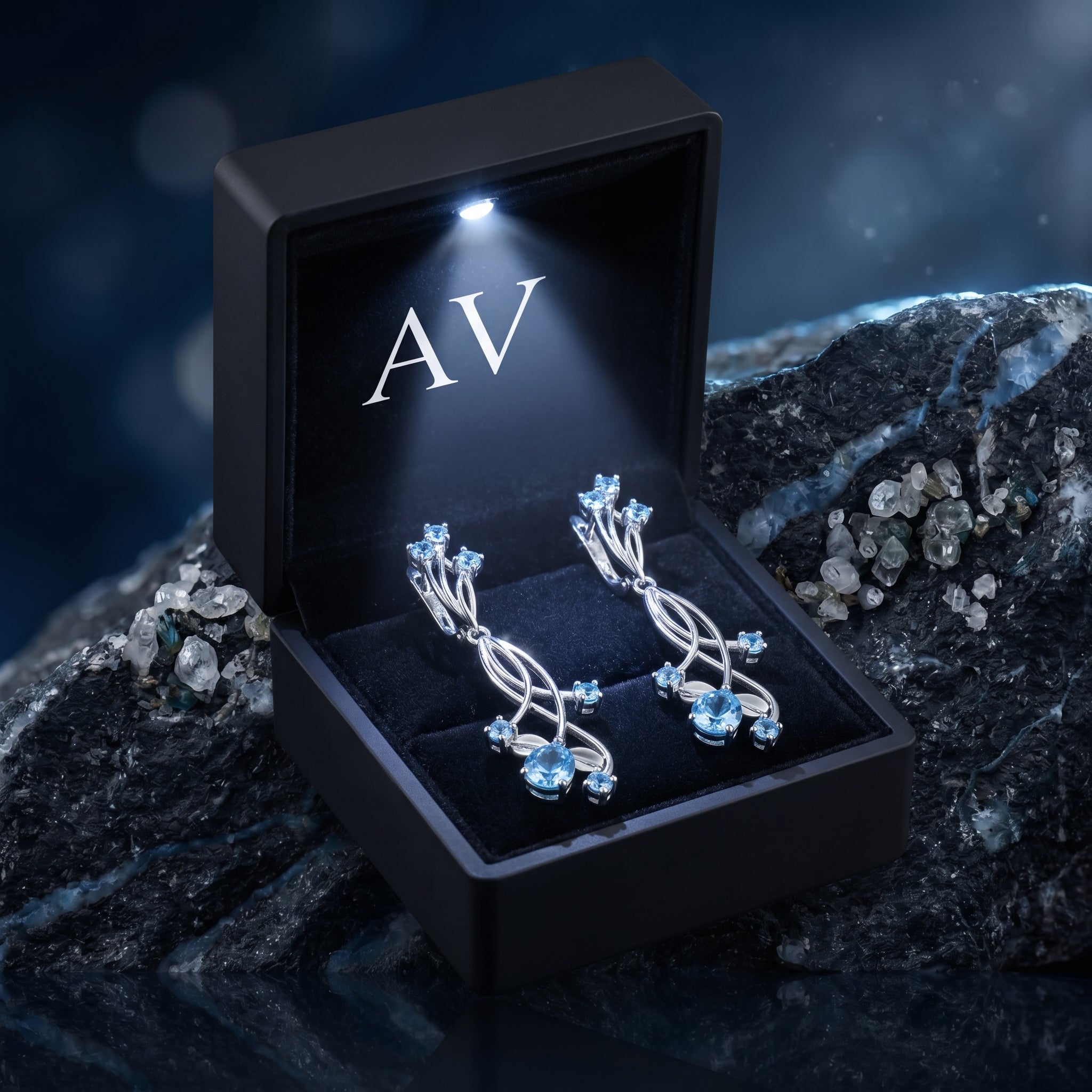 Oceanis Cascade silver blue topaz drop earrings in a luxury black LED-lit gift box on a dark stone surface.